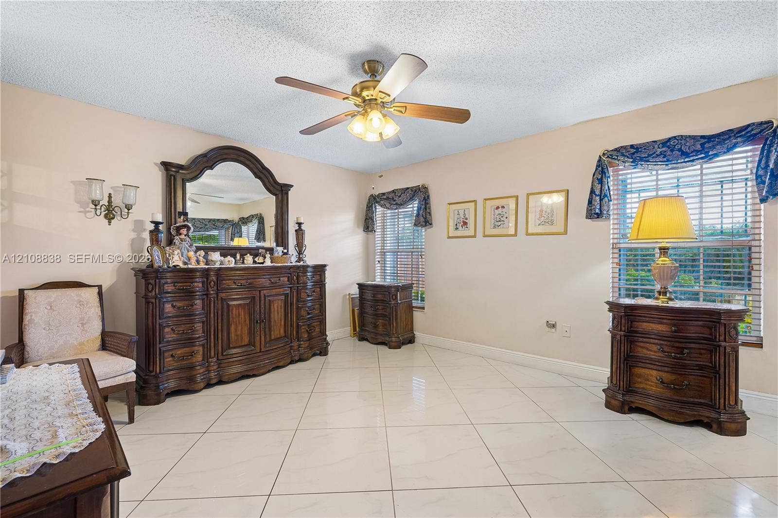 Large-format neutral tile flooring, ceiling fan with integrated light fixture, dual wall-mounted light sconces, and double-pane windows with horizontal blinds