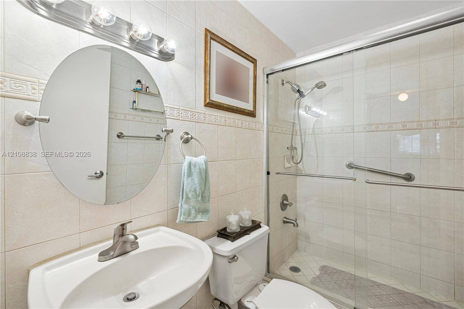 Bathroom featuring ceramic wall tiling with decorative trim, oval vanity mirror, brushed-nickel hardware, and a walk-in shower enclosure with a sliding glass door