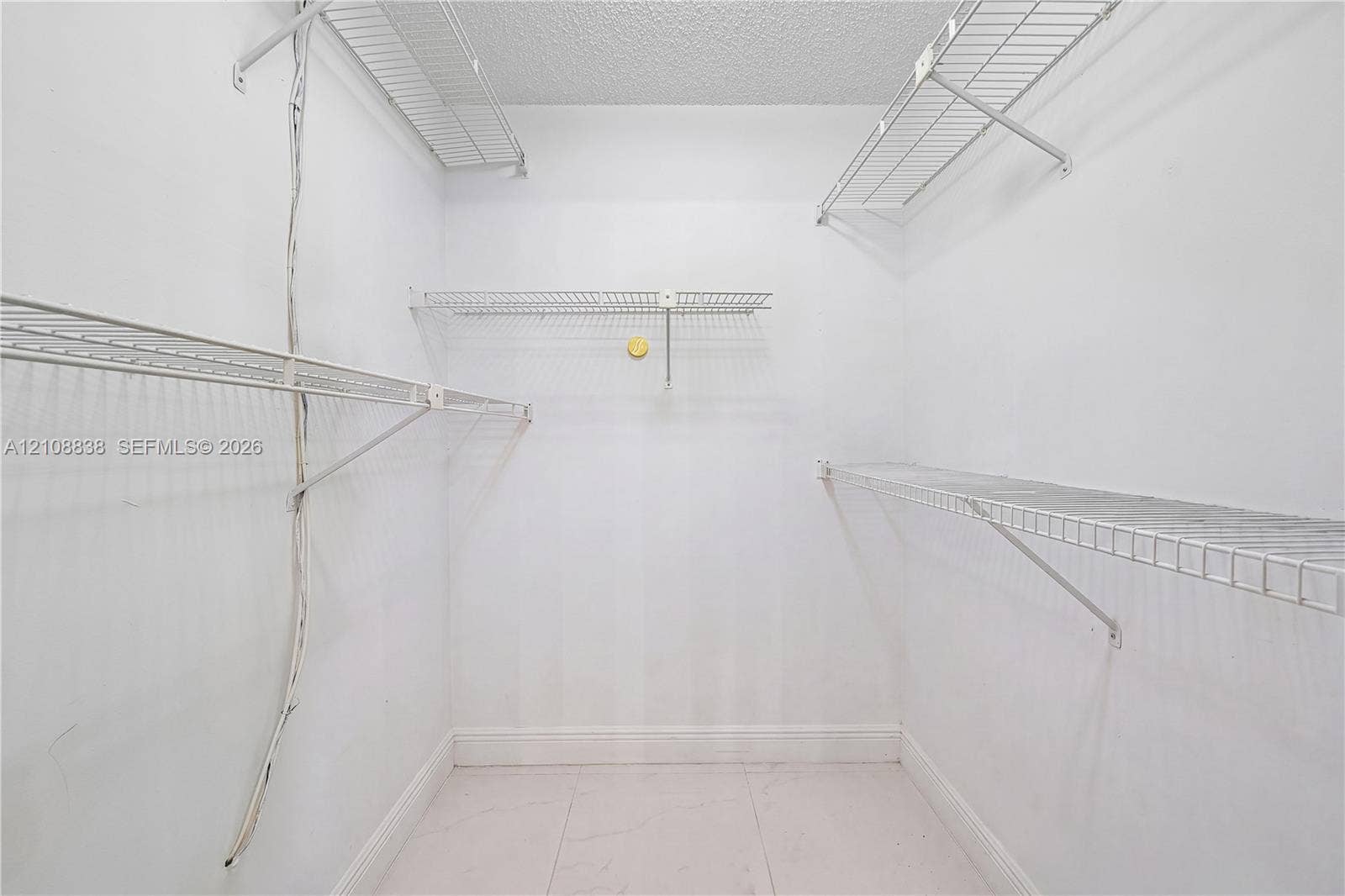 Walk-in storage space featuring white walls, large-format tile flooring, and multi-level white wire shelving