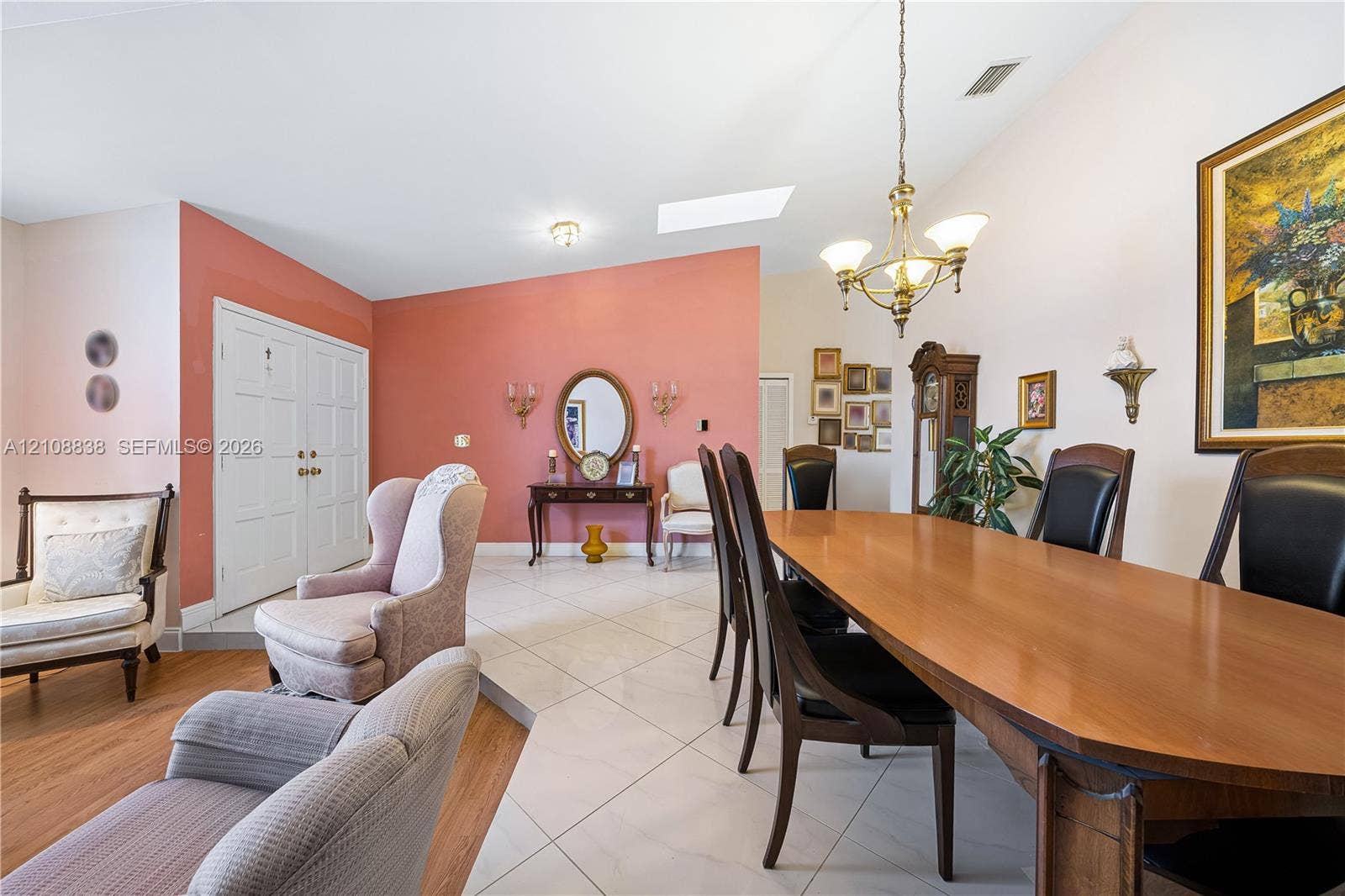 Open-concept area featuring vaulted ceilings, oversized tile flooring, wood-finish flooring, a skylight, and a decorative chandelier