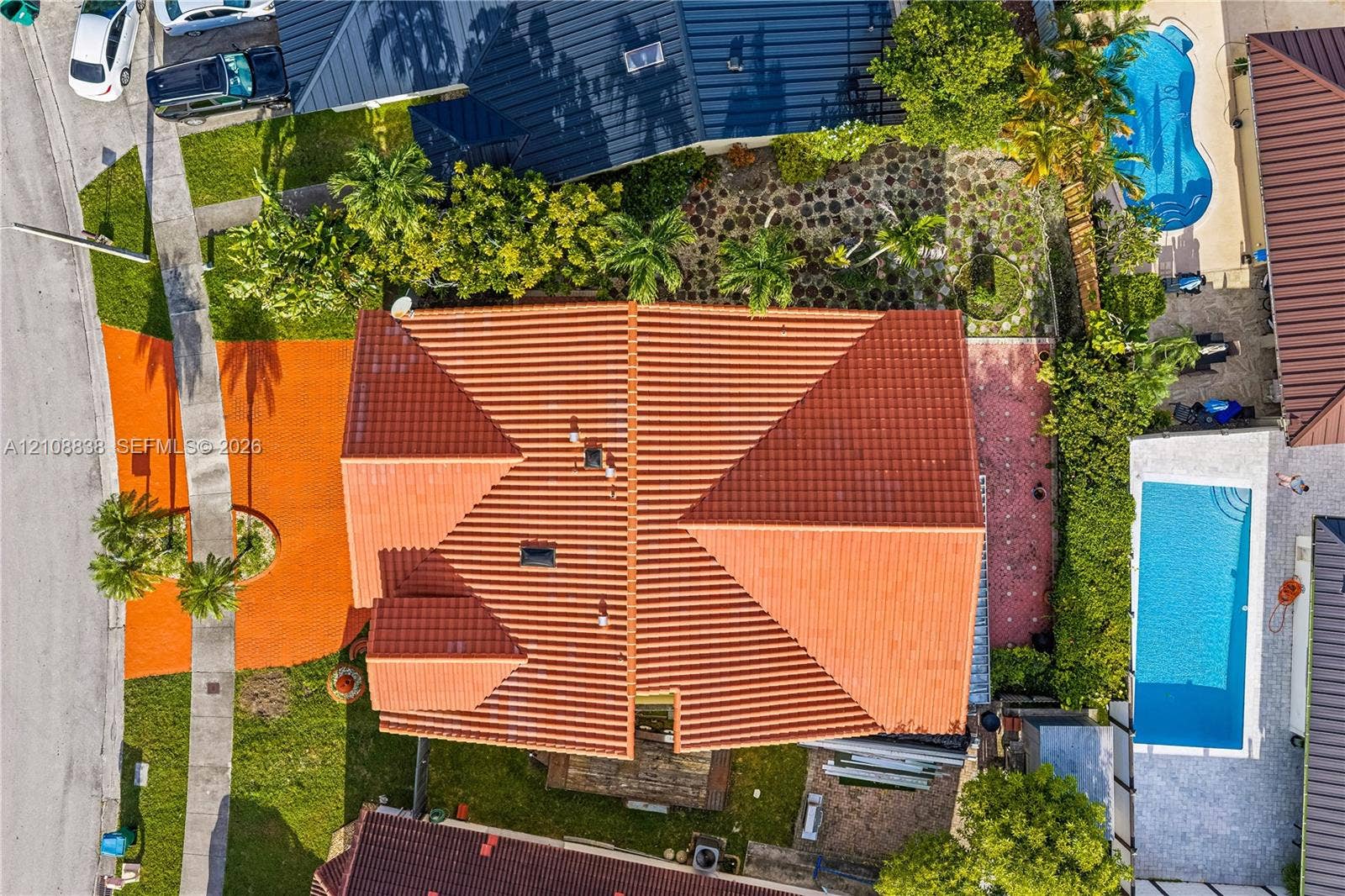 Aerial view of a property featuring a multi-pitched clay tile roof, a private swimming pool, landscaped lawn, and decorative stone paving