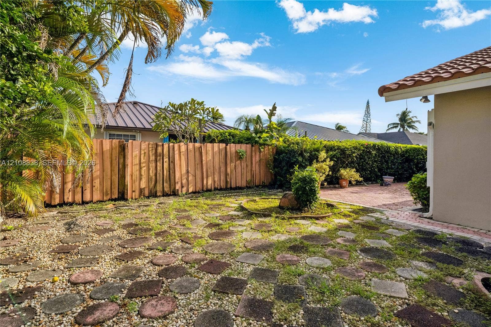 Rear exterior featuring a wood-plank privacy fence, stone-paver hardscaping, brick-paved patio area, and mature perimeter landscaping