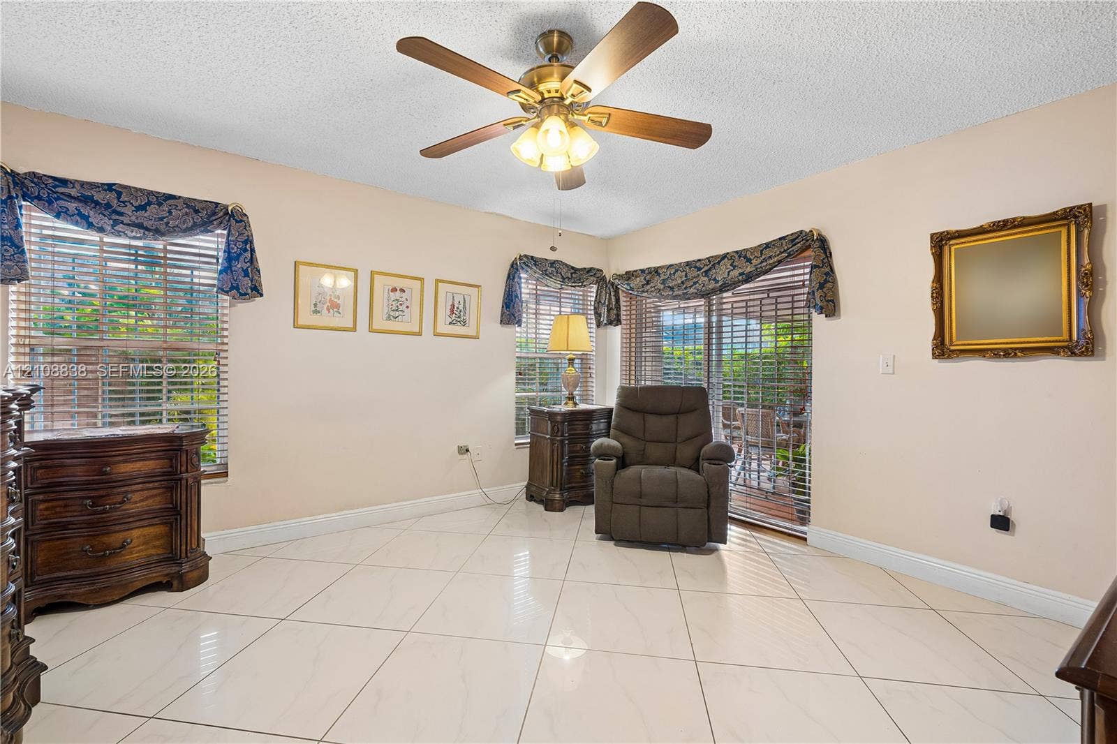 Large-format light-toned tile flooring, multi-pane windows with horizontal blinds, central ceiling fan with integrated lighting, and glass sliding door providing outdoor access