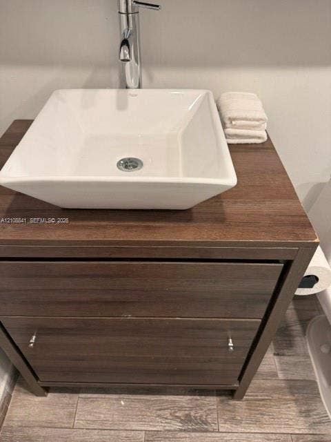 Vanity featuring a wood-finish cabinet with dual drawers, a square ceramic vessel sink, and a chrome single-handle faucet