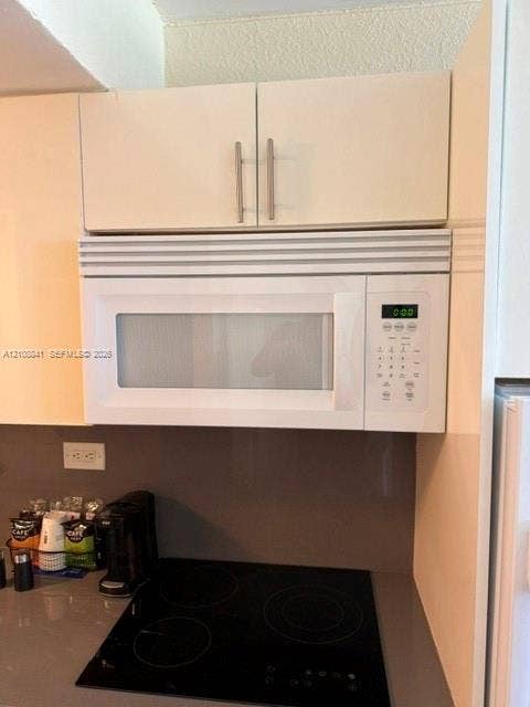 Built-in over-the-range microwave, flat-panel cabinetry with brushed-metal pulls, and a smooth-surface electric cooktop set into a solid-surface countertop