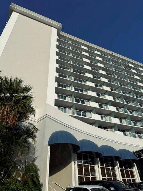 High-rise building exterior featuring tiered balconies with glass railings, structural columns, and arched blue awnings