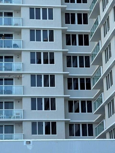 High-rise exterior featuring a light gray facade, multi-level balconies with glass railings, and expansive rectangular windows