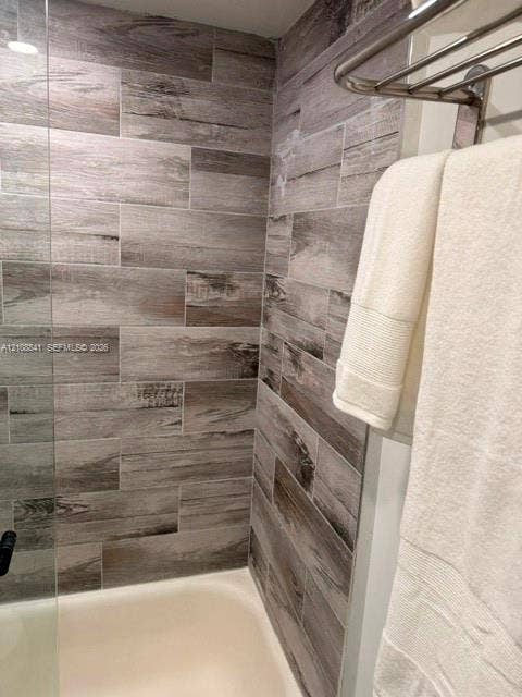 Shower enclosure featuring wood-finish tile wall surfacing, a glass panel, and a stainless steel wall-mounted rack