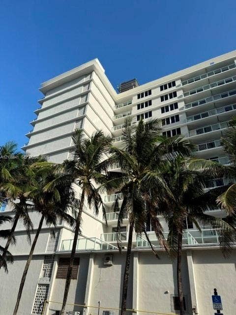 High-rise residential exterior featuring white concrete facade, multi-level private balconies with glass railings, and structural geometric accents