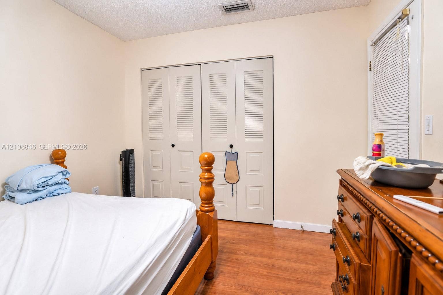 11827 SW 99th Lane, Miami, FL 33186 Wood-finish flooring, dual-panel closet doors with louvered upper sections, and a window fitted with horizontal blinds