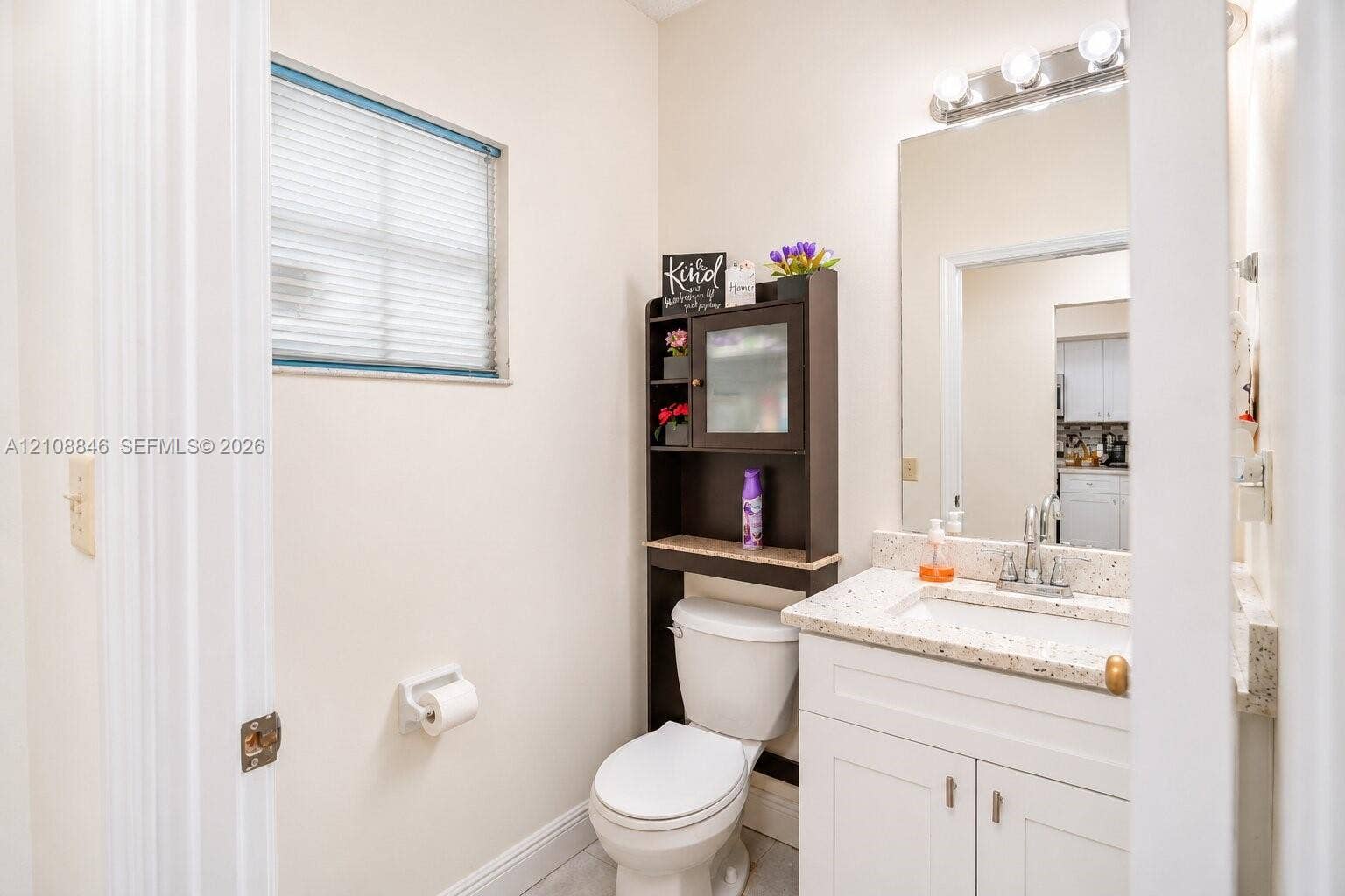 11827 SW 99th Lane, Miami, FL 33186 Bathroom featuring a vanity with a white cabinet and stone-composite countertop, integrated sink, wall-mounted mirror, four-bulb light fixture, and horizontal blind window