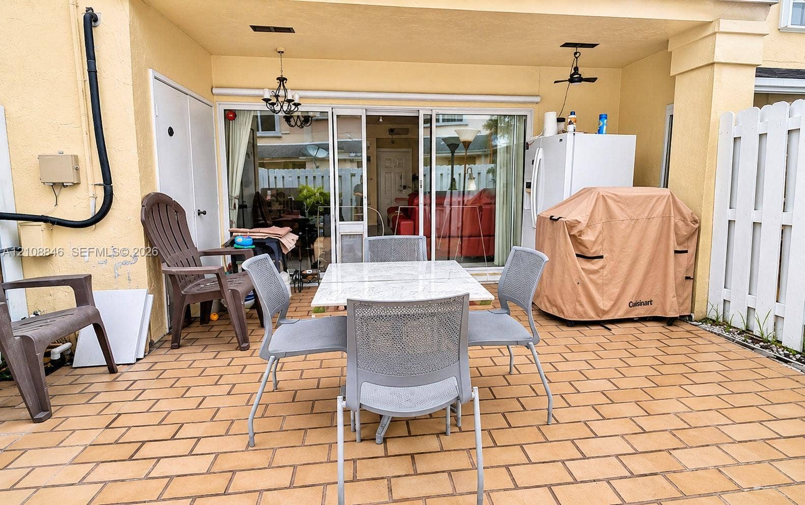 11827 SW 99th Lane, Miami, FL 33186 Covered patio featuring brick-style paver flooring, sliding glass doors, built-in storage closet, and white privacy fencing
