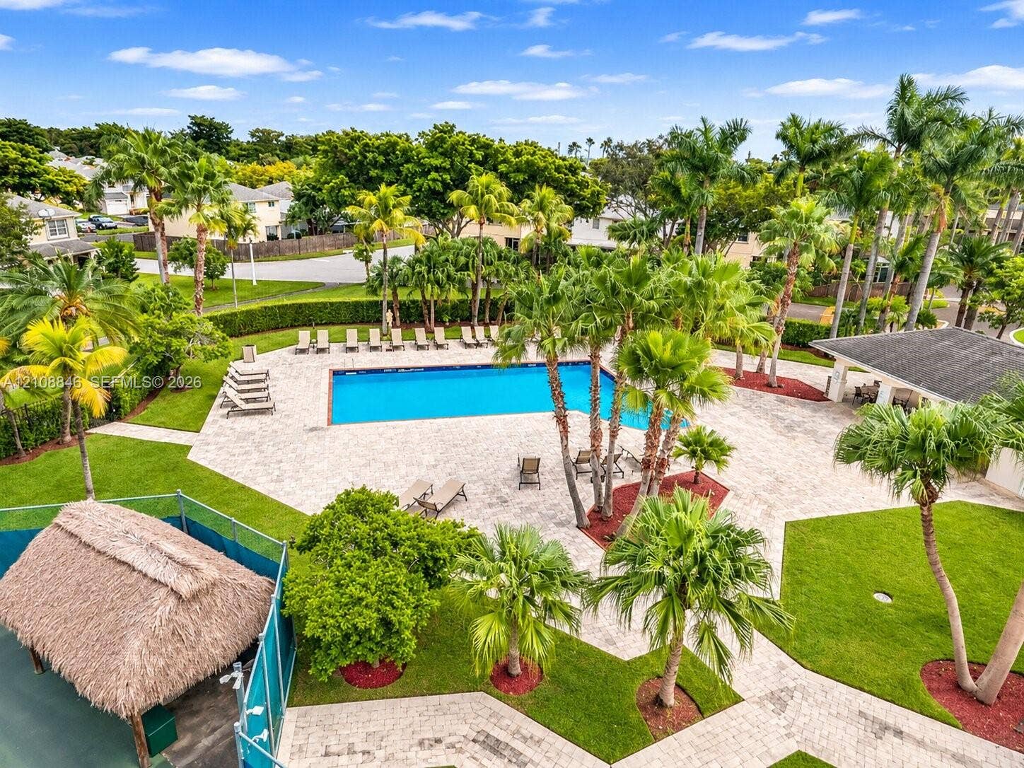 11827 SW 99th Lane, Miami, FL 33186 Community swimming pool featuring a paved deck, surrounding mature palm trees, manicured lawns, and a thatched-roof pavilion