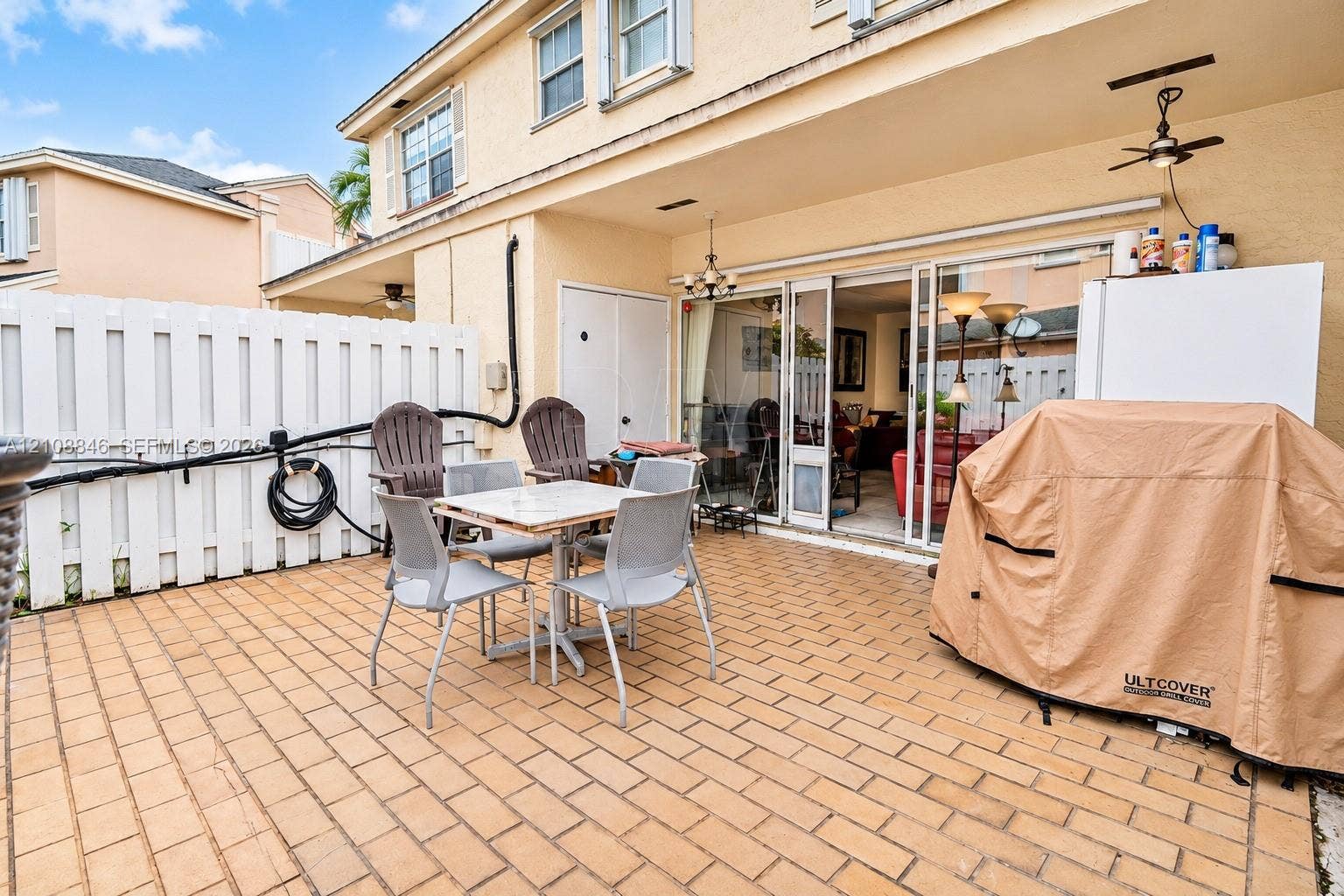 11827 SW 99th Lane, Miami, FL 33186 Covered concrete patio with paver-style finish, multi-panel sliding glass doors, white vinyl privacy fencing, and ceiling-mounted light fixtures