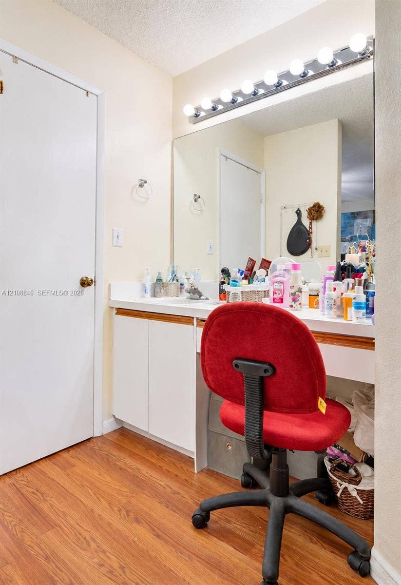11827 SW 99th Lane, Miami, FL 33186 Built-in vanity featuring white cabinetry, a solid surface countertop, an expansive wall-to-wall mirror, integrated multi-bulb vanity lighting, and wood-finish flooring