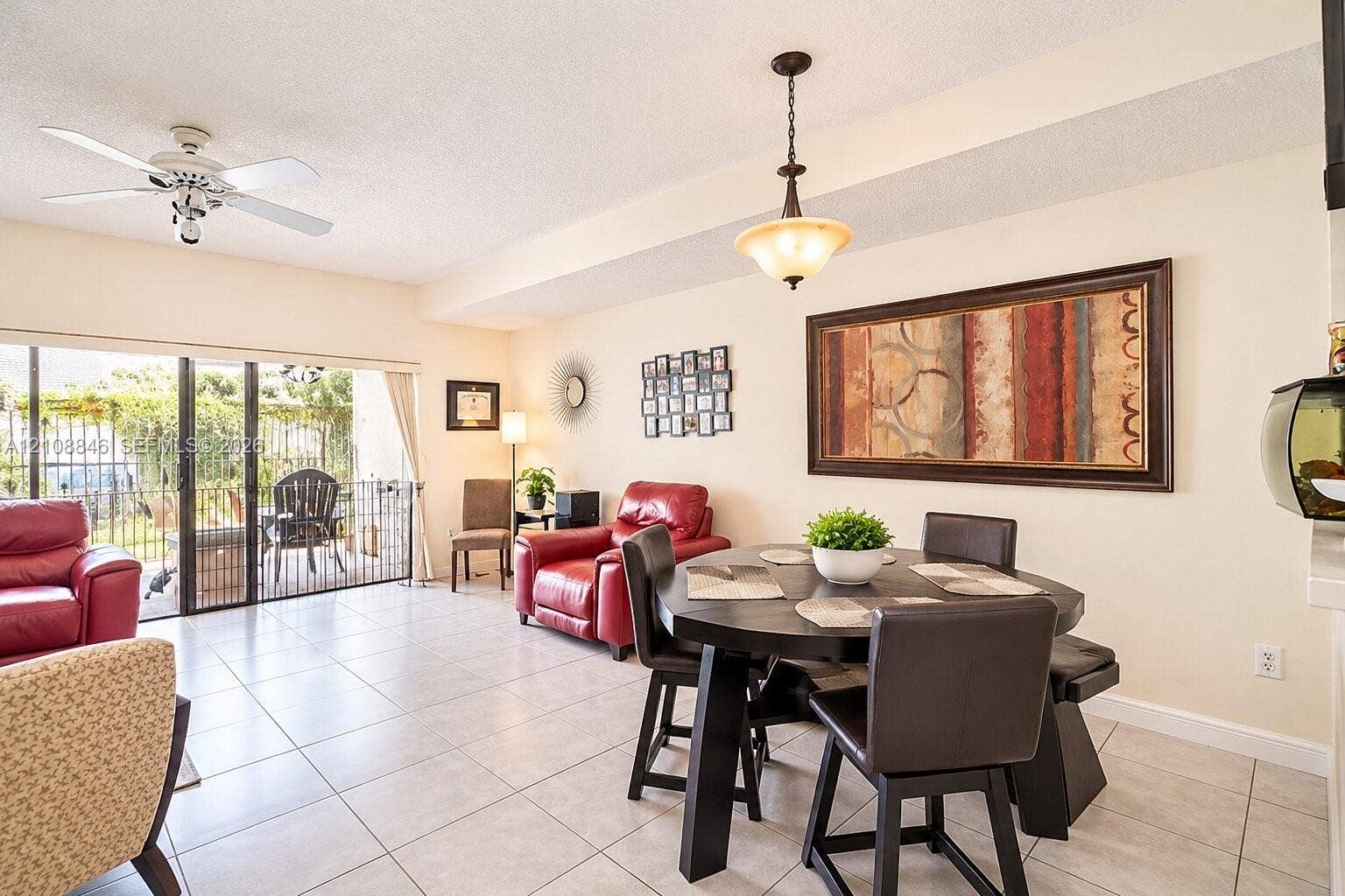 11827 SW 99th Lane, Miami, FL 33186 Open living area featuring neutral tile flooring, a ceiling fan with integrated lighting, a bowl-style pendant light fixture, and sliding glass doors