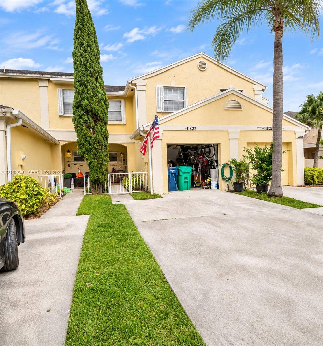11827 SW 99th Lane, Miami, FL 33186 Stucco exterior townhouse featuring a two-car garage, concrete driveway, and front gated courtyard