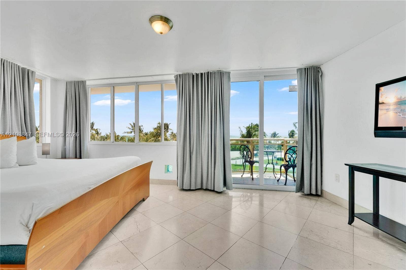 Light-colored stone tile flooring, expansive wall-to-wall glass windows, and sliding glass doors with access to an exterior balcony