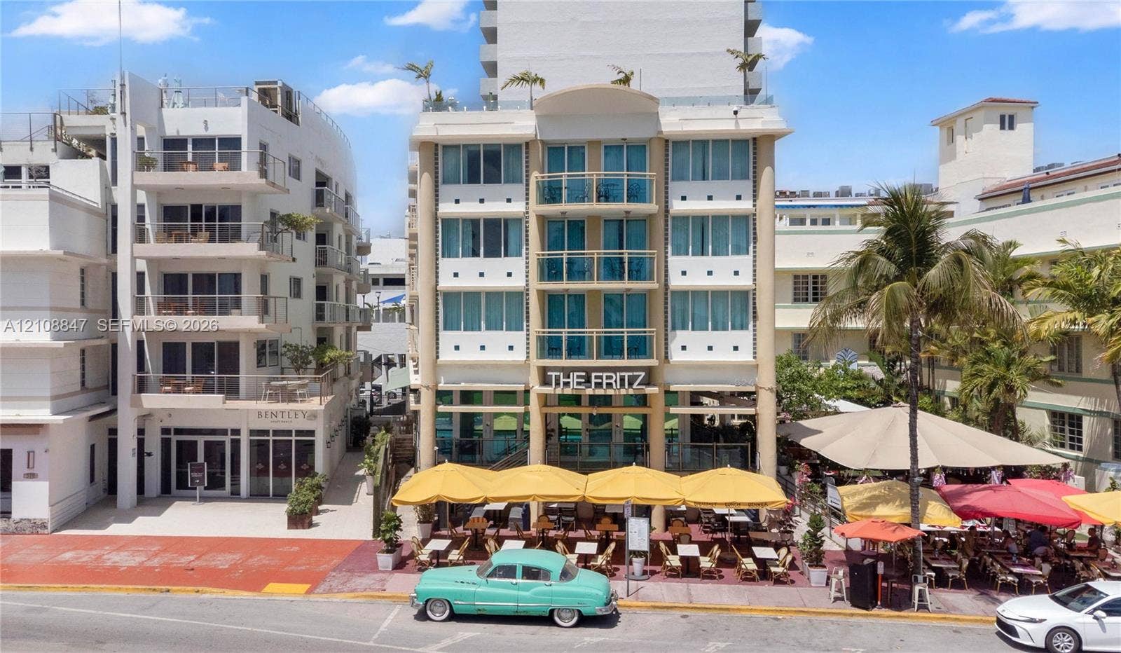 Multi-story building exterior featuring Art Deco architectural details, glass-paneled balconies, floor-to-ceiling windows, and a ground-level covered terrace