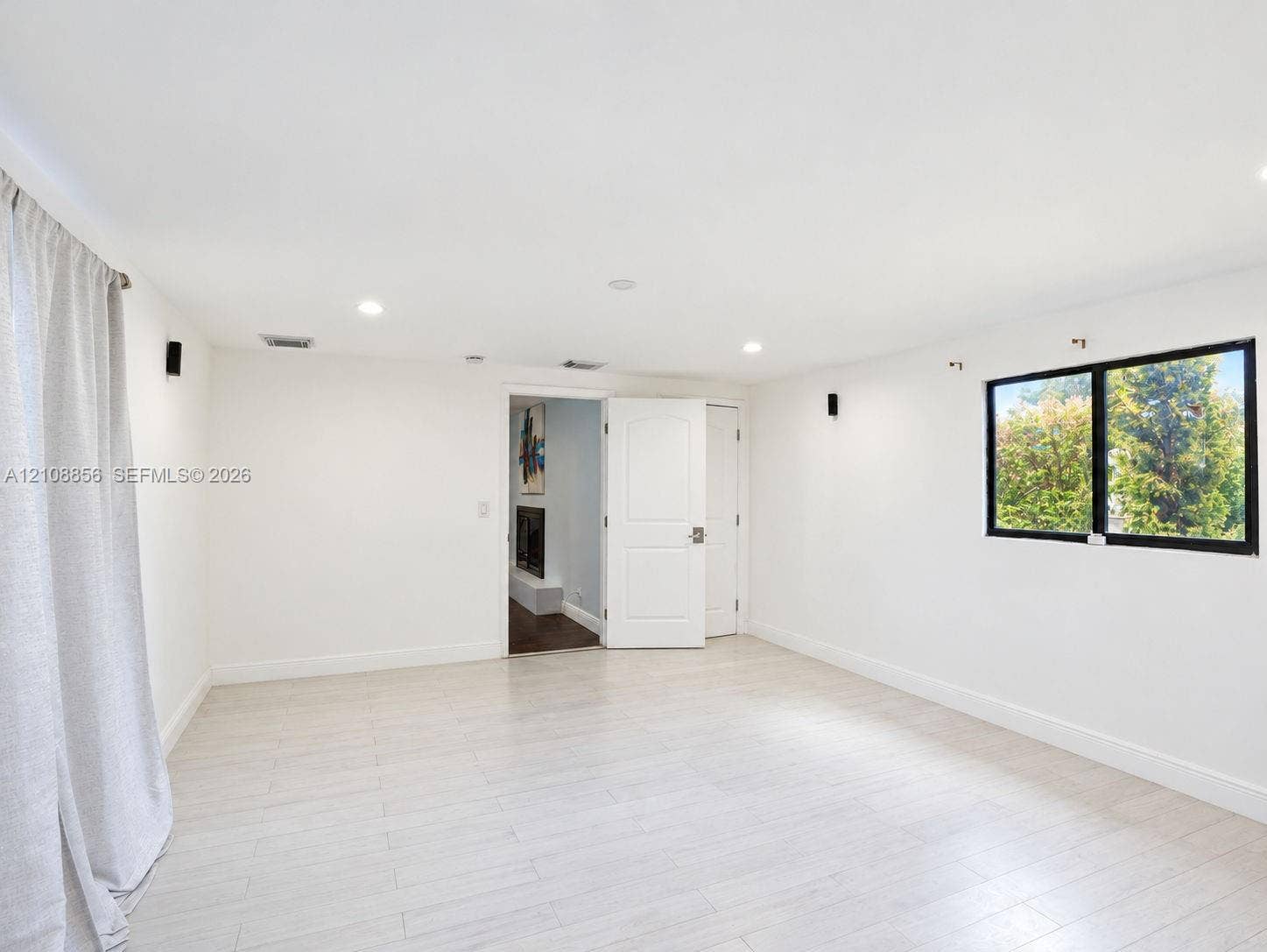 Neutral-toned space featuring light-colored wood-finish flooring, recessed lighting, and a window with a black frame