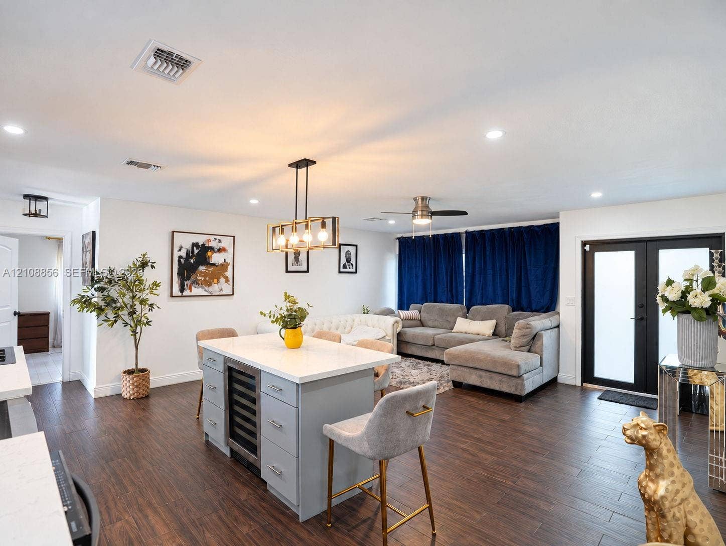 Open-concept living space featuring wood-finish flooring, recessed lighting, a central kitchen island with integrated wine refrigeration and stone-finish countertop, and black-framed glass double entry doors