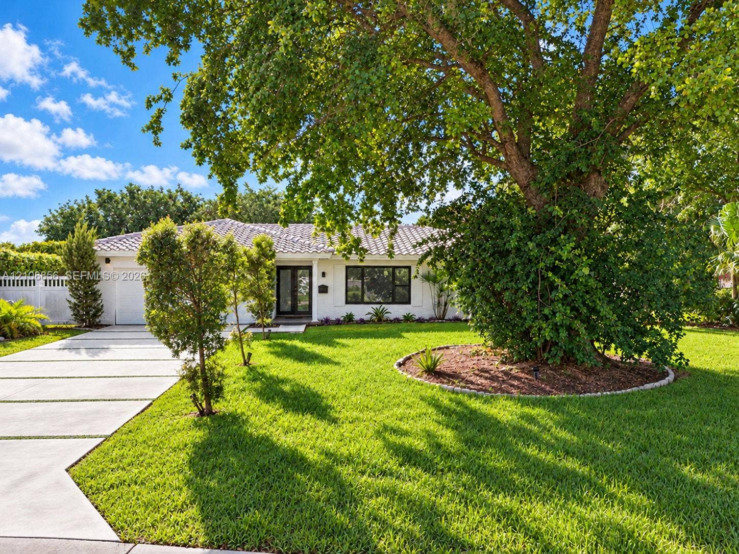 Single-story exterior featuring a light-toned facade, tile roof, concrete paver driveway, and mature landscaping with established trees