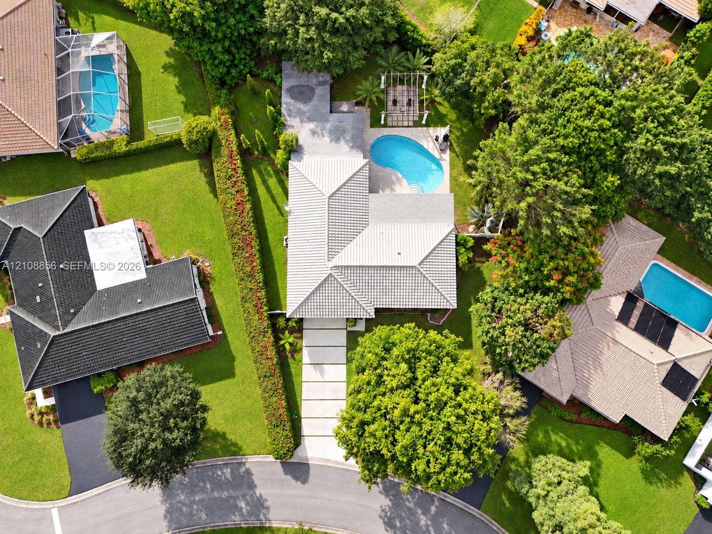 Aerial perspective featuring a concrete tile roof, curvilinear swimming pool, pergola, and a multi-section concrete paver driveway