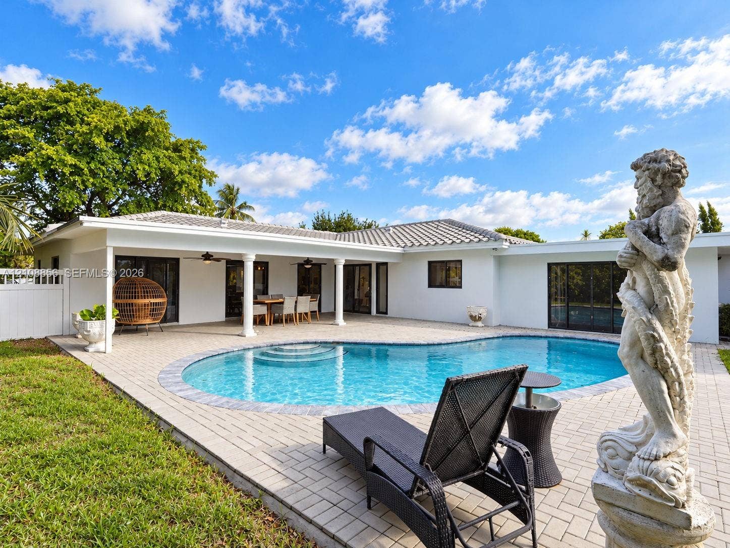 Backyard featuring a curved inground pool, expansive paver patio, covered porch with column supports, and manicured lawn