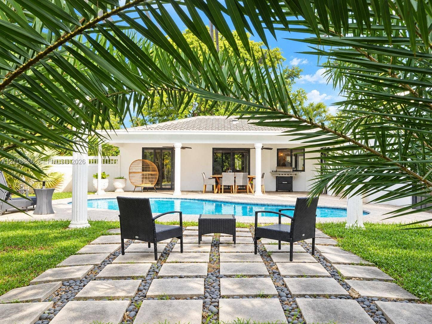 Outdoor space featuring a swimming pool, concrete paver grid patio with stone inlay, covered patio area, and architectural columns