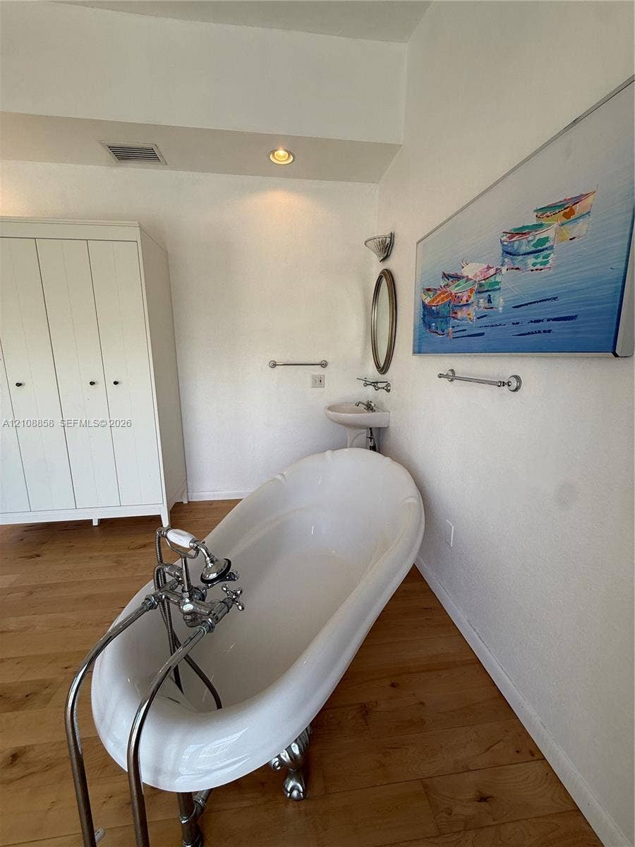 Clawfoot soaking tub with polished chrome hardware, wood-finish flooring, pedestal sink, and built-in white cabinetry
