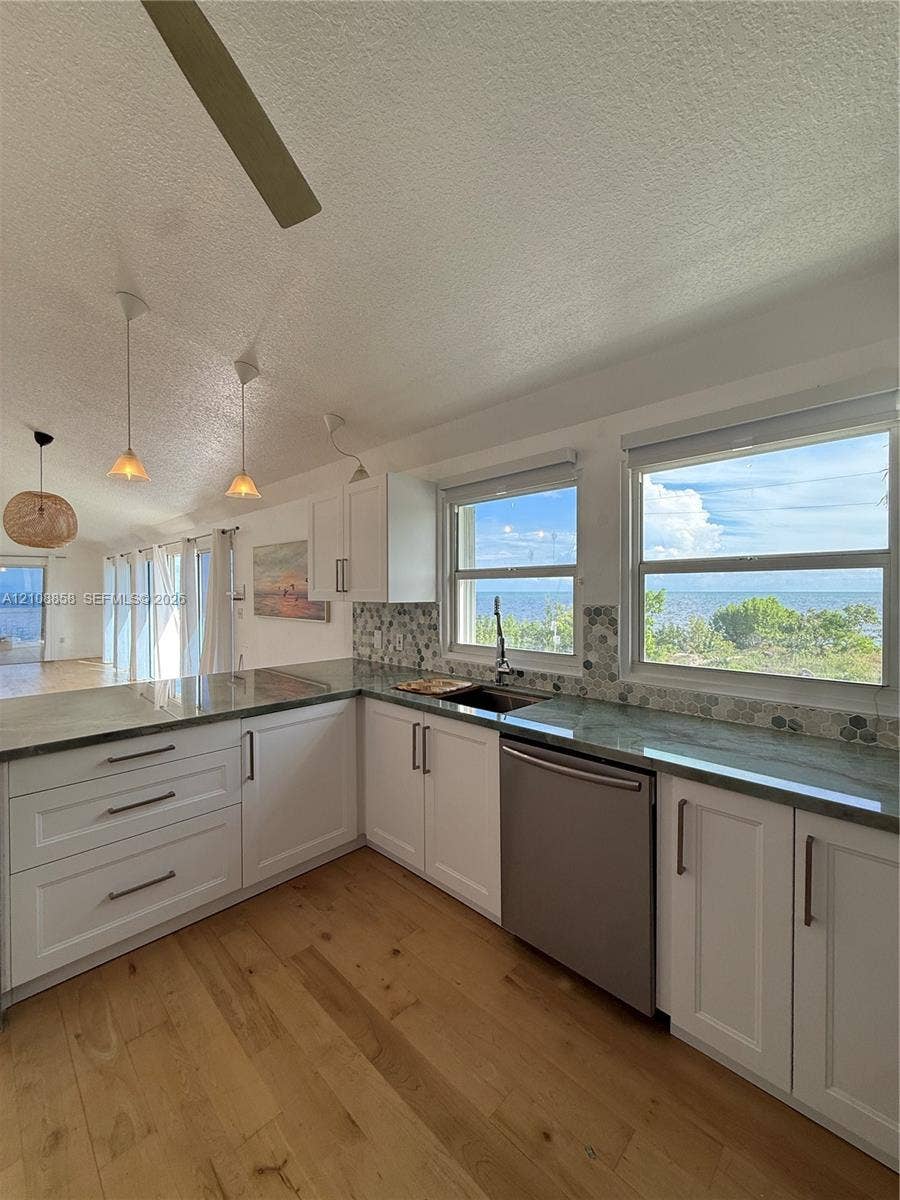 Kitchen featuring white shaker-style cabinetry, stone-finish countertops, stainless steel dishwasher, hexagonal tile backsplash, and wood-finish flooring
