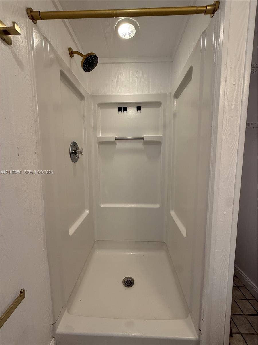 Shower stall with white molded surround, built-in shelving, brass-finish shower head, and recessed ceiling lighting