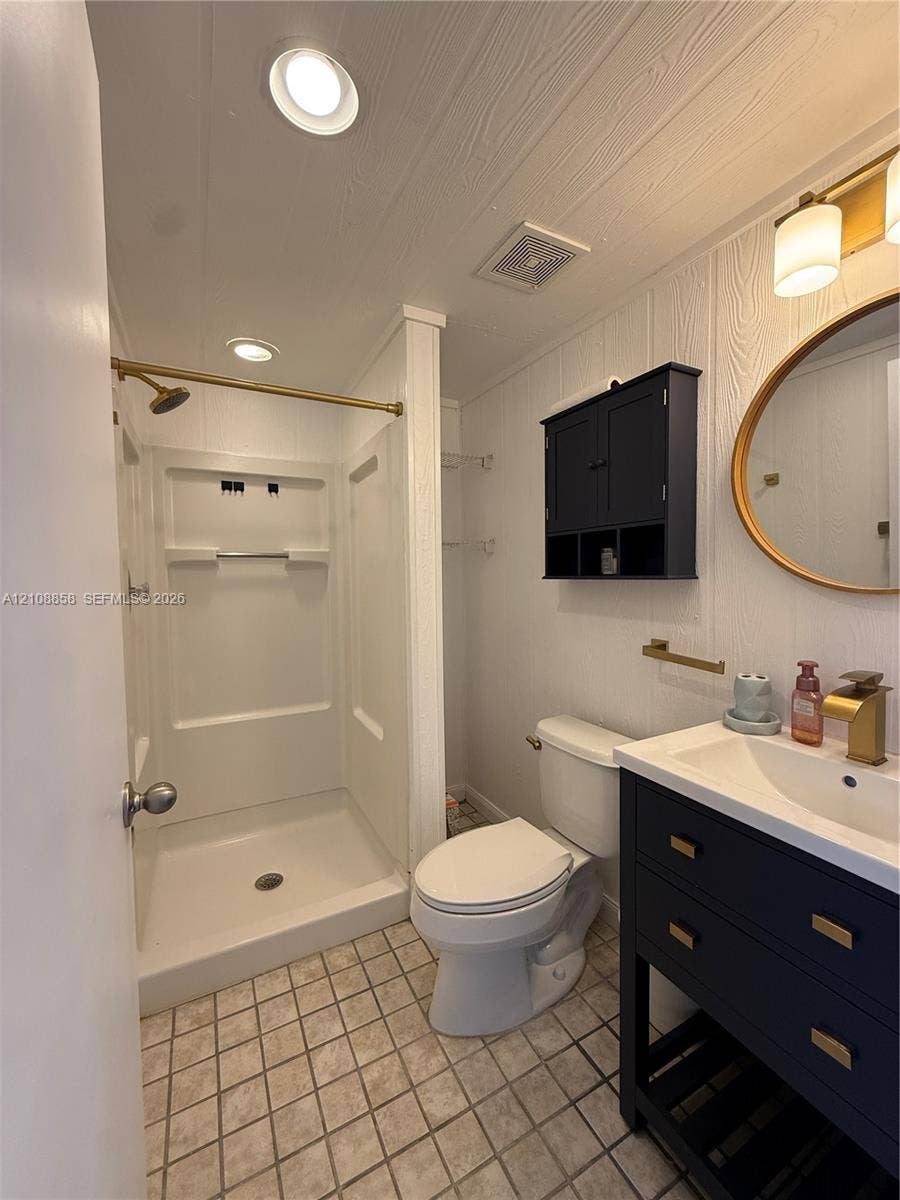Bathroom featuring a dark-toned vanity with integrated basin, brass-finish fixtures, oval wall mirror, built-in cabinet storage, and a walk-in shower enclosure