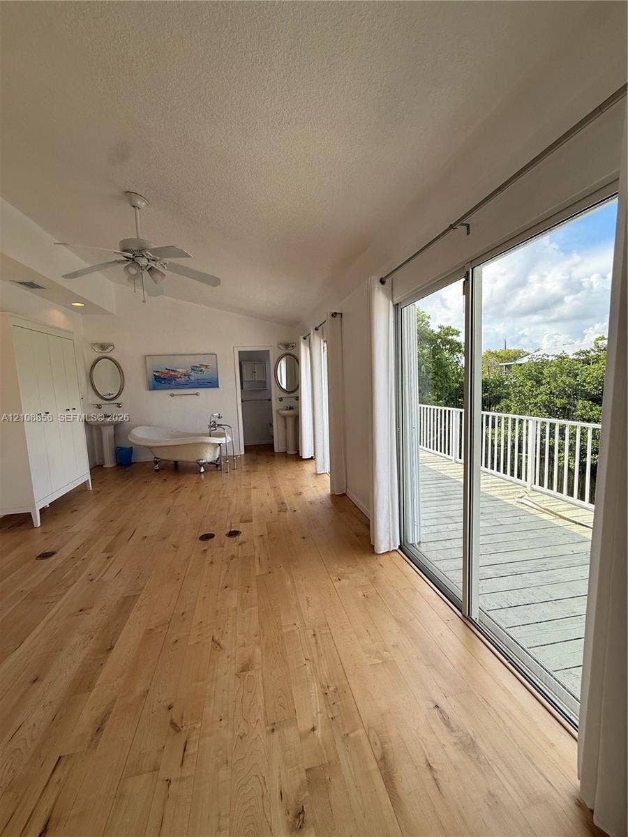 Wood-finish flooring, freestanding soaking tub, dual pedestal sinks with oval mirrors, and large sliding glass doors opening to a railed exterior deck