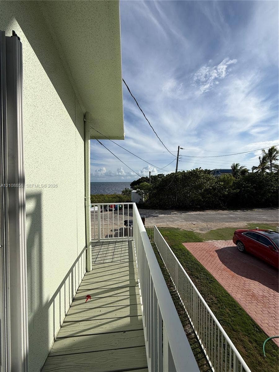 Elevated balcony featuring a painted wood-finish deck and white metal railings with water and horizon scenery