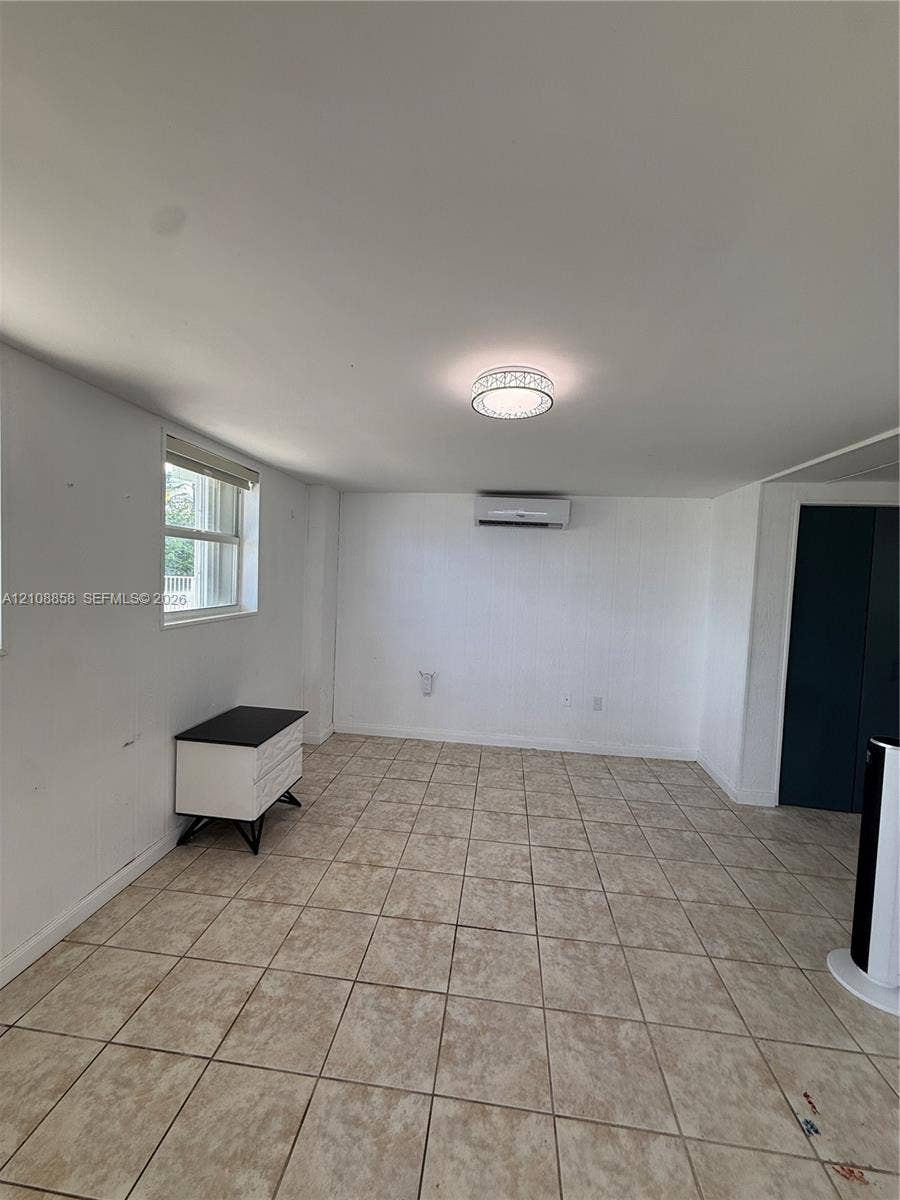 Interior space featuring neutral tile flooring, a wall-mounted mini-split HVAC system, a flush-mount circular light fixture, and a window with a horizontal blind