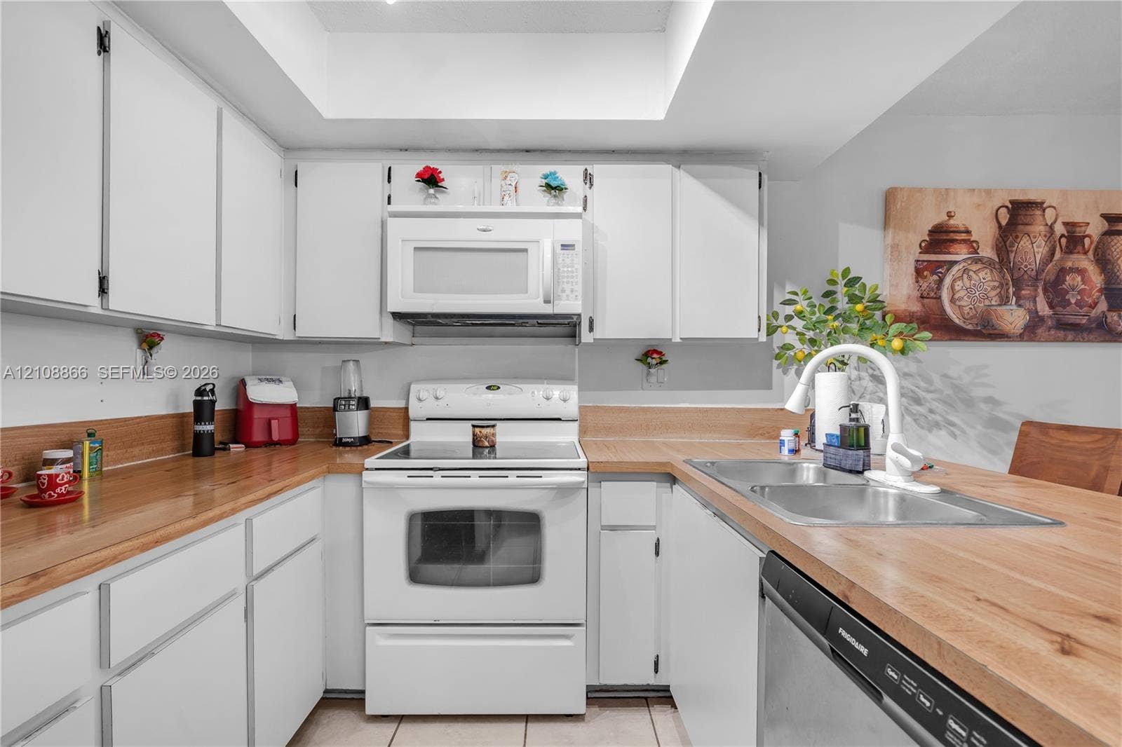 10859 NW 7th Street, #21-18, Miami, FL 33172 Kitchen featuring white shaker-style cabinetry, wood-finish countertops, tile flooring, a dual-basin stainless steel sink with a high-arch faucet, and an integrated white microwave
