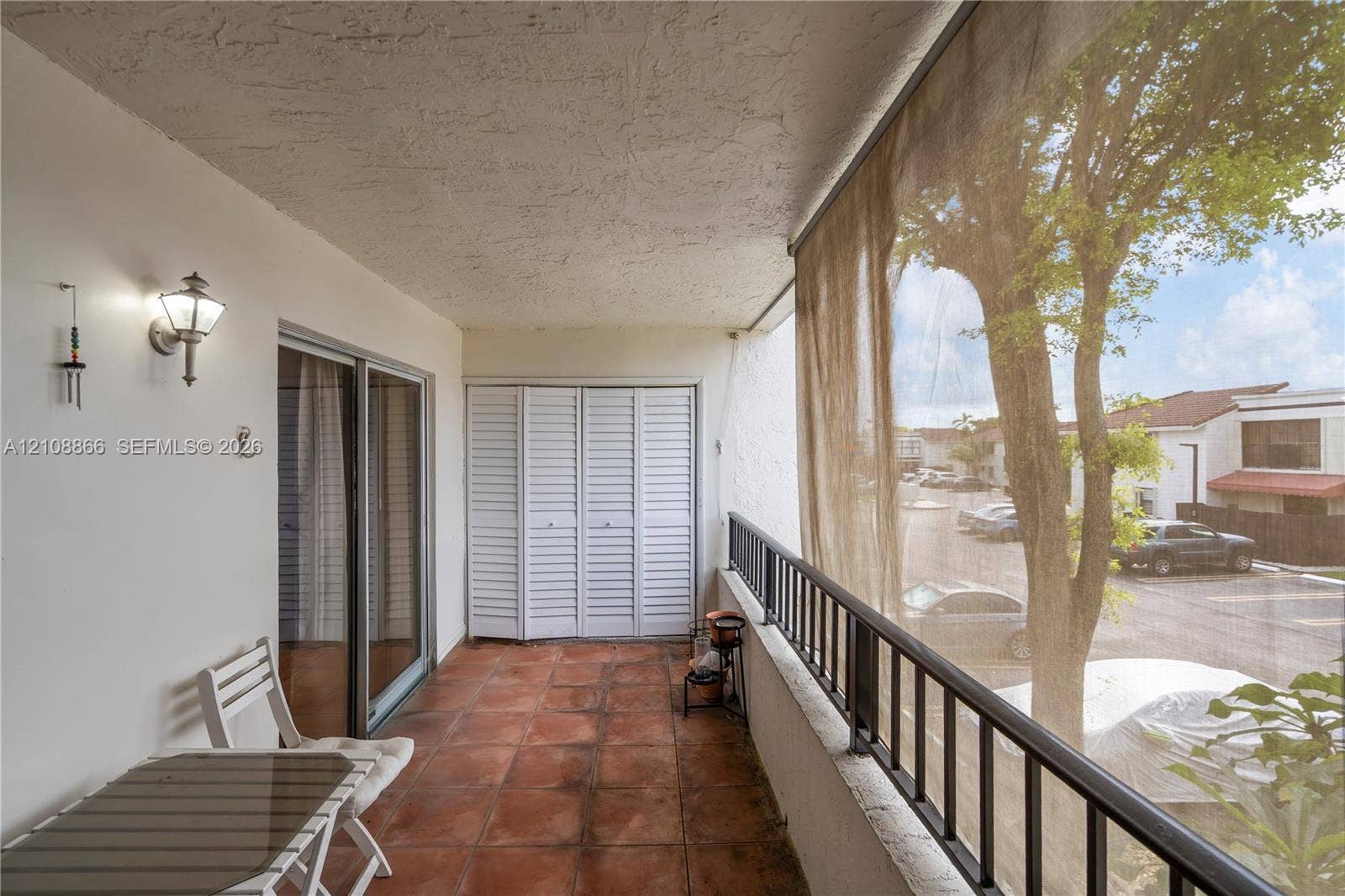 10859 NW 7th Street, #21-18, Miami, FL 33172 Covered balcony featuring terracotta-style tile flooring, white bi-fold doors, a black metal railing, and an exterior wall-mounted lantern light