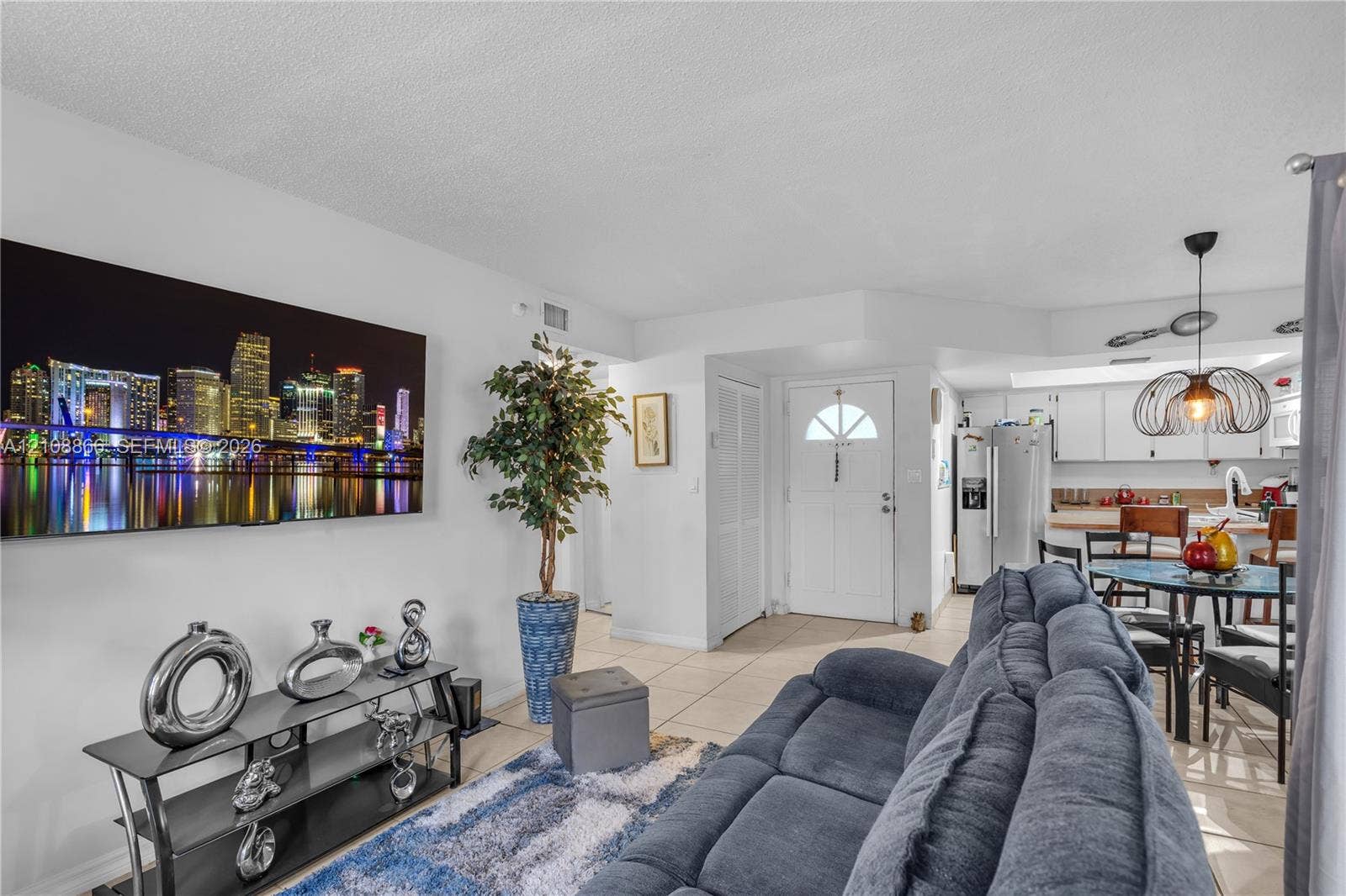 10859 NW 7th Street, #21-18, Miami, FL 33172 Open-concept area featuring neutral tile flooring, white cabinetry, a kitchen island, and a distinctive pendant light fixture