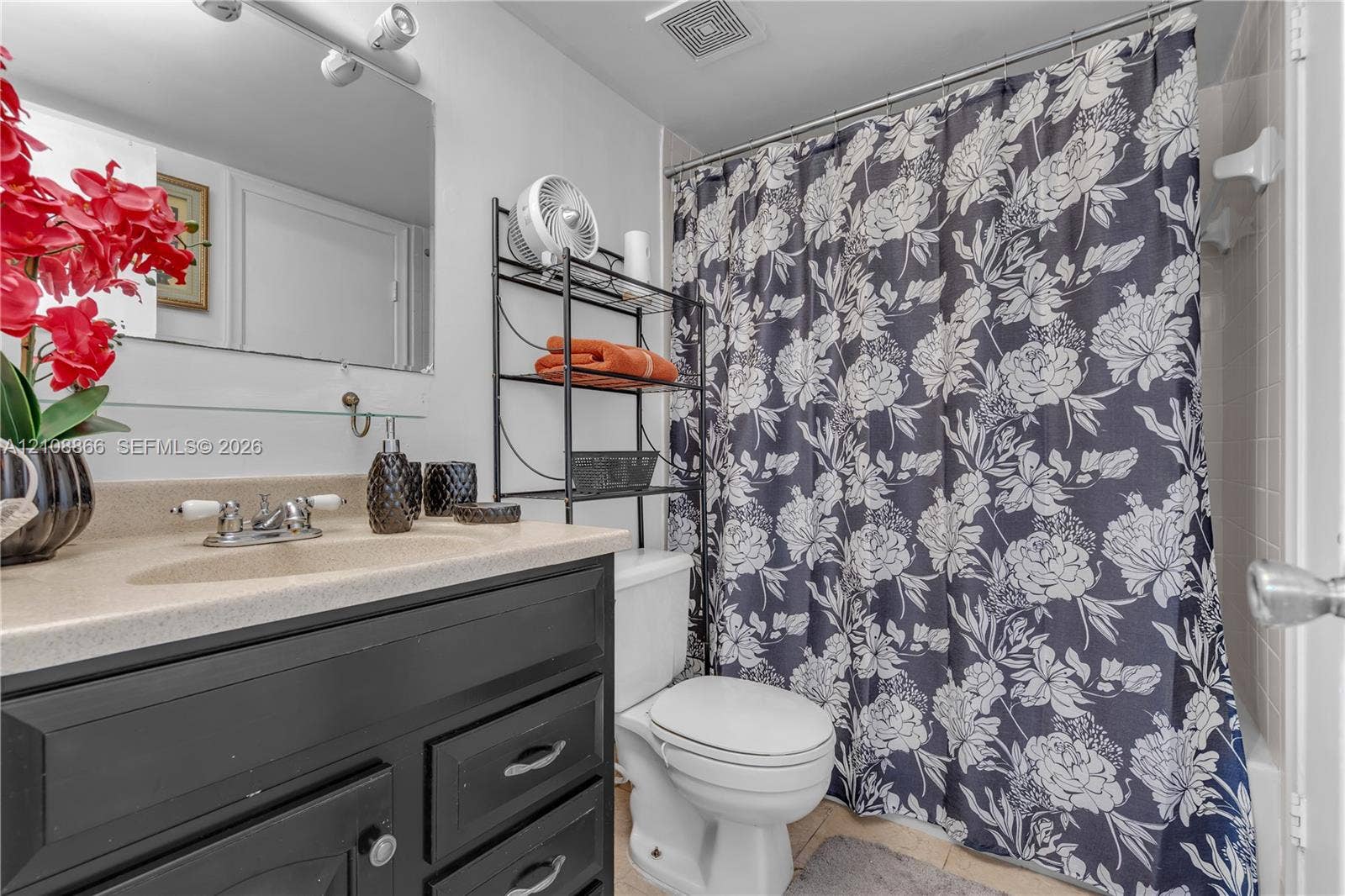 10859 NW 7th Street, #21-18, Miami, FL 33172 Bathroom featuring a black vanity with a molded countertop and integrated sink, chrome dual-handle faucet, wall-mounted mirror, and a tiled tub enclosure