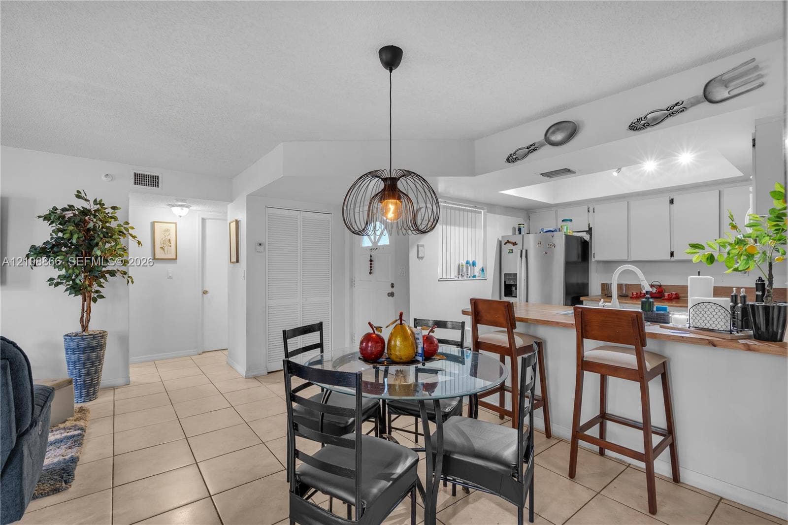 10859 NW 7th Street, #21-18, Miami, FL 33172 Open-concept kitchen featuring a breakfast bar with wood-finish countertop, white cabinetry, tile flooring, and a modern wire-frame pendant light