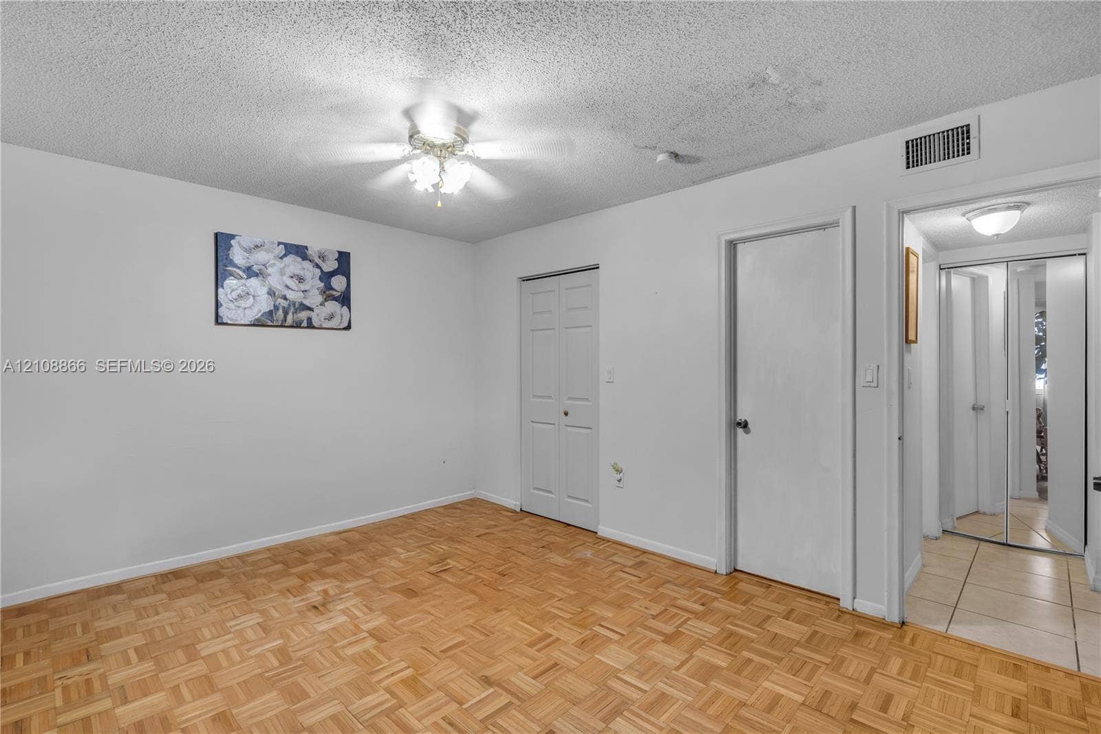 10859 NW 7th Street, #21-18, Miami, FL 33172 Parquet wood-finish flooring, white walls, built-in dual-panel closet doors, and a ceiling-mounted light fixture with a fan