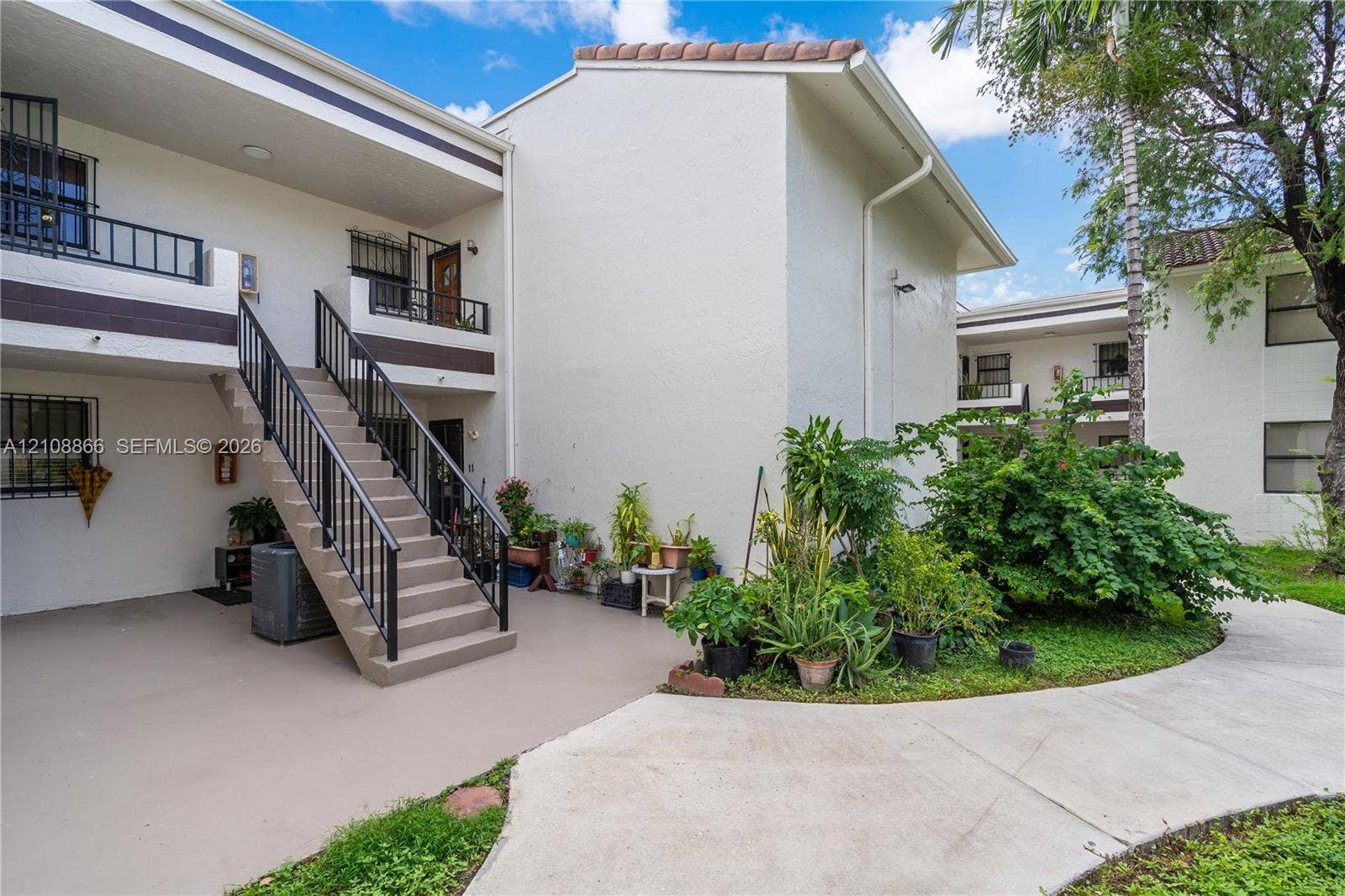 10859 NW 7th Street, #21-18, Miami, FL 33172 Stucco exterior with multi-level balconies, metal railings, exterior staircase, concrete walkways, and mature landscaping