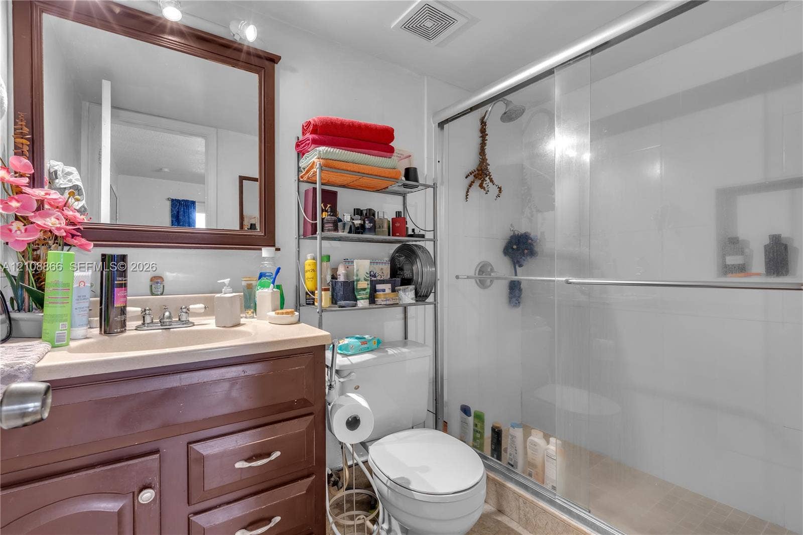 10859 NW 7th Street, #21-18, Miami, FL 33172 Bathroom featuring a dark wood-finish vanity, integrated sink, framed wall mirror, and a walk-in shower with a glass sliding door and built-in shelving niche