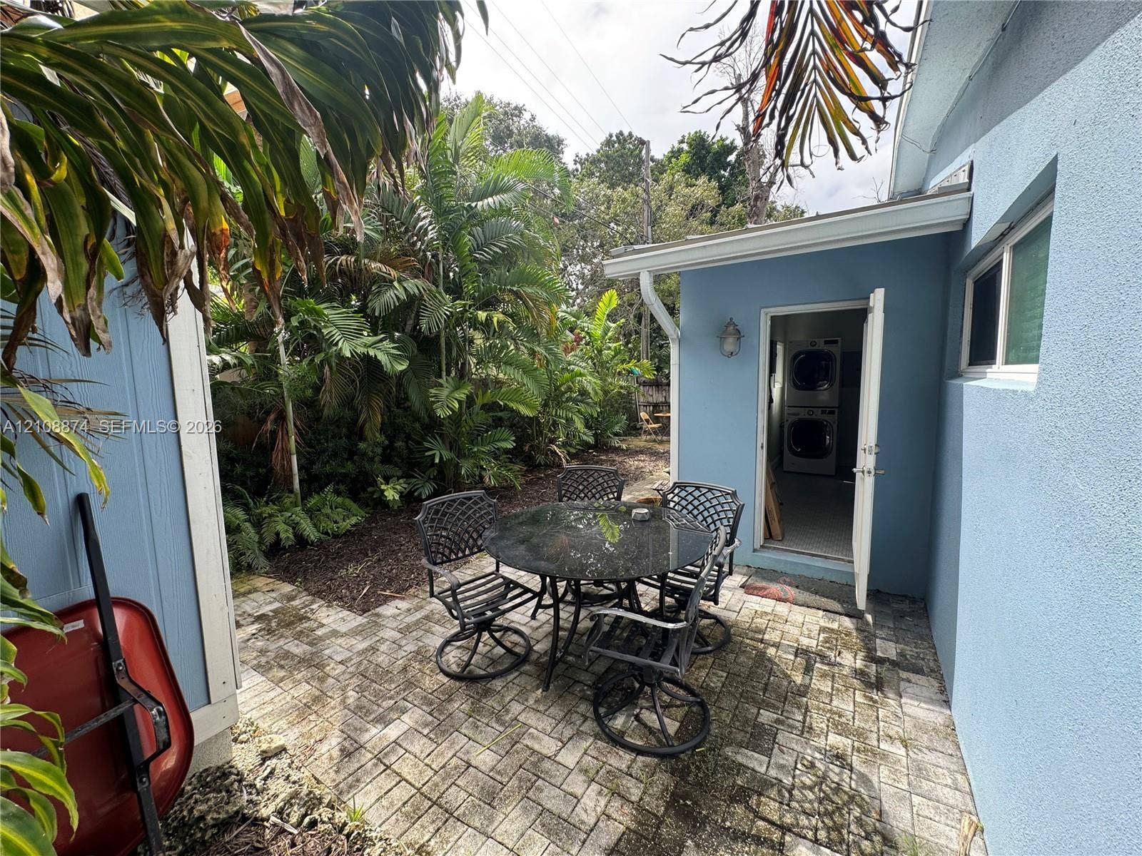 Paved patio featuring a herringbone brick pattern, stucco exterior walls, and a dedicated laundry area with an external entry door