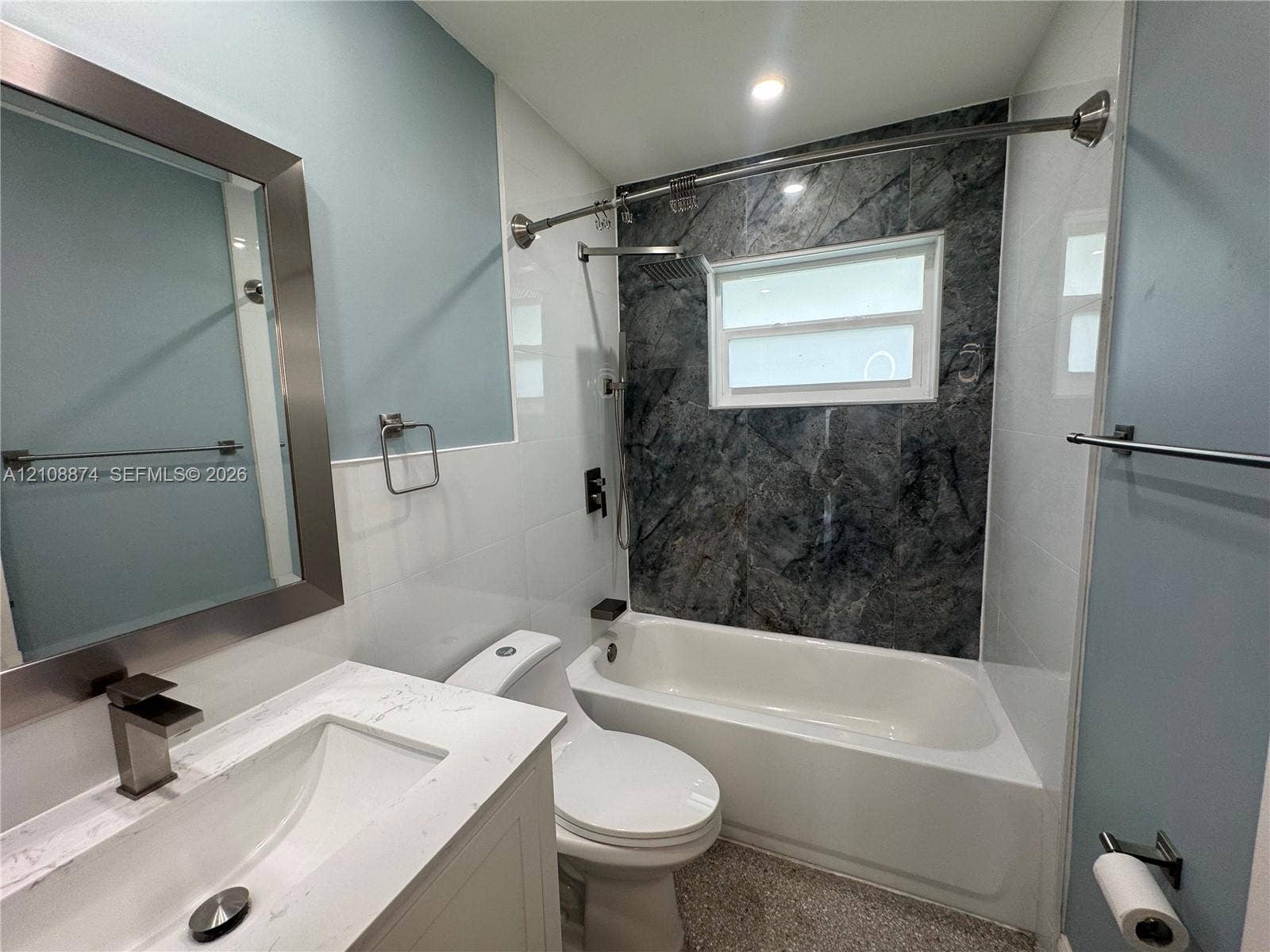 Bathroom featuring a white vanity with a stone-top integrated sink, a deep soaking tub with a patterned tile surround, and a framed mirror with metallic finish
