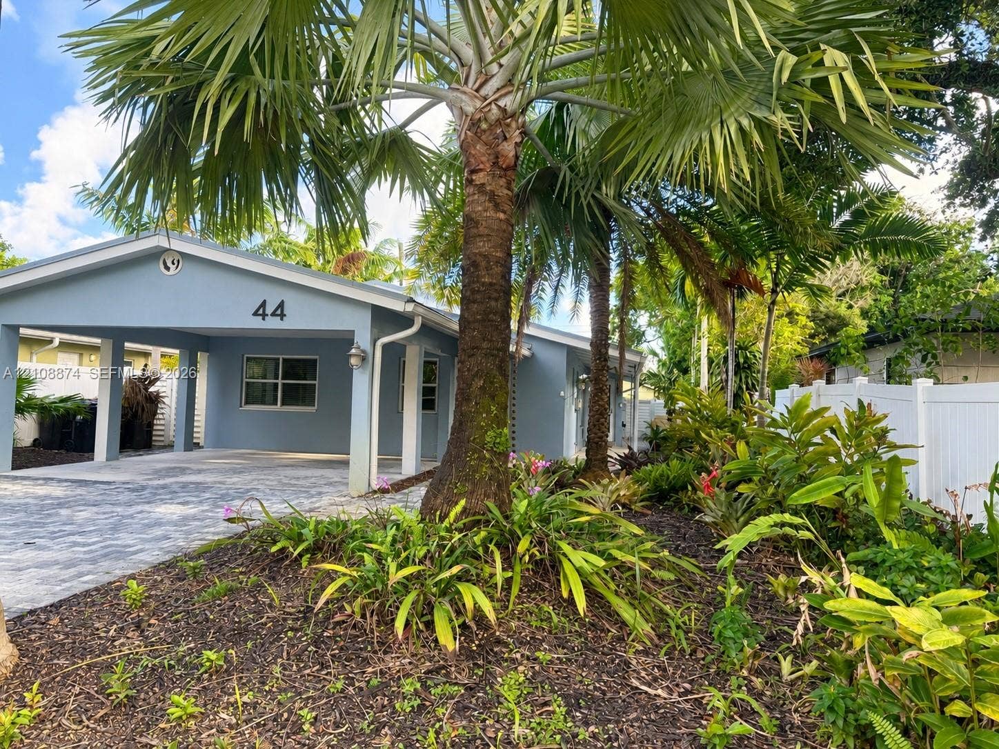 44 NE 16th Court, #2, Fort Lauderdale, Fort Lauderdale, FL 33305 Exterior featuring a covered carport, paver driveway, mature palm trees, and white vinyl privacy fencing