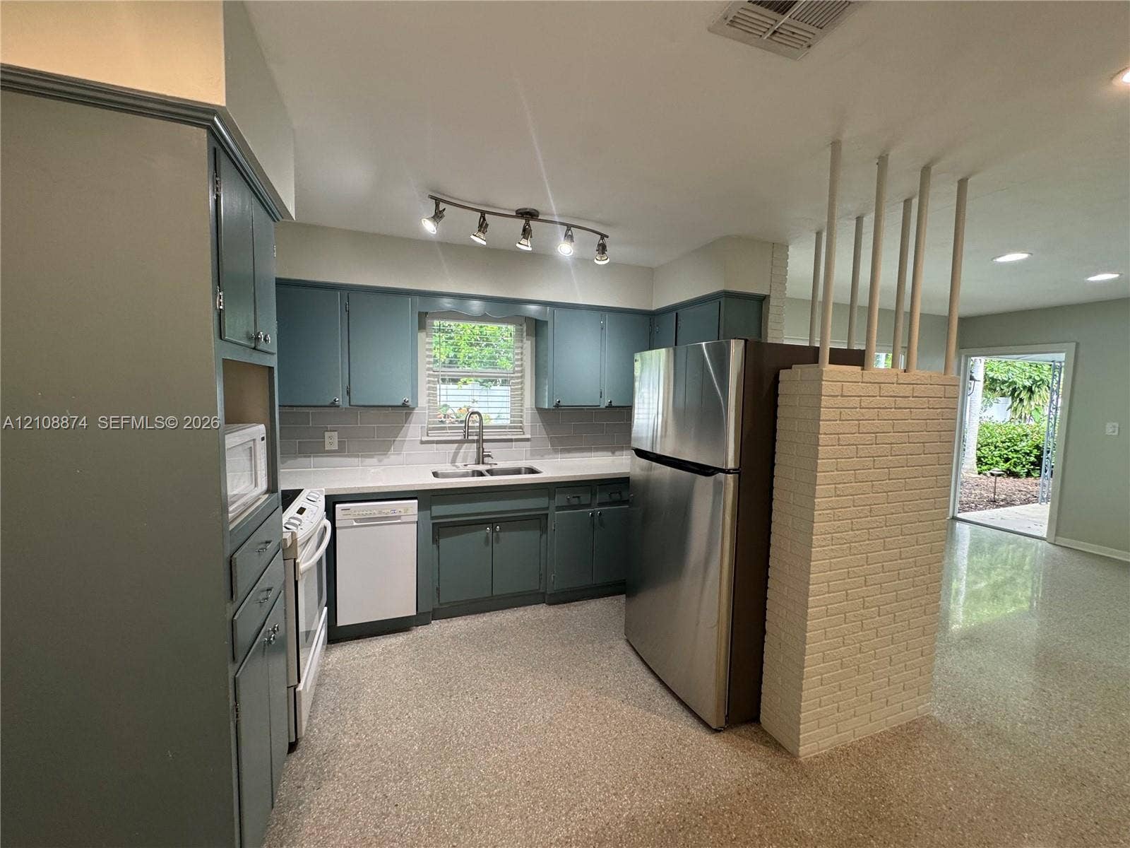 Kitchen featuring blue cabinetry, stone-surface countertops, tile backsplash, stainless steel appliances, and a white brick partition wall