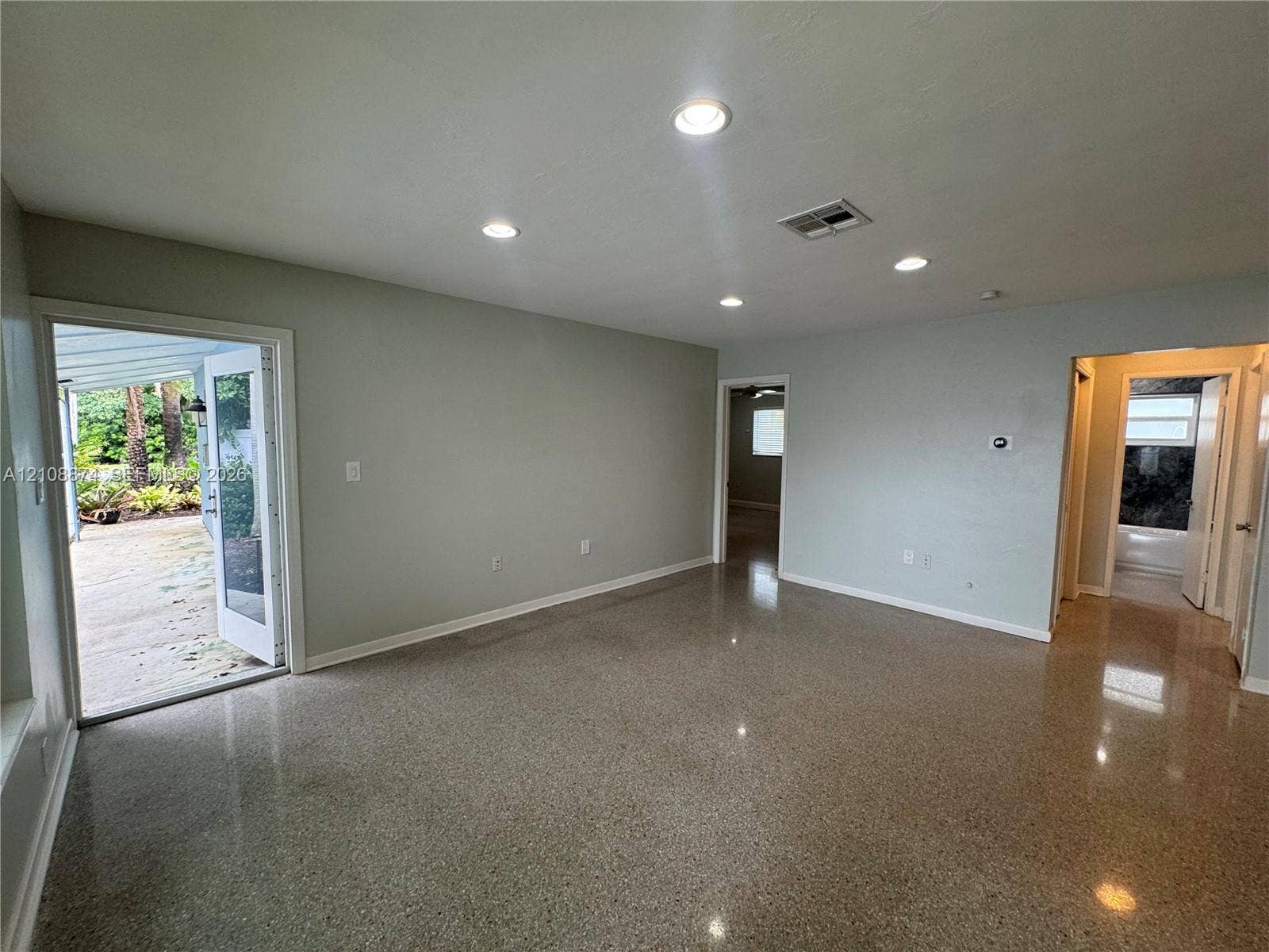 Polished terrazzo flooring, recessed lighting, and a glass-paneled door opening to an exterior concrete patio