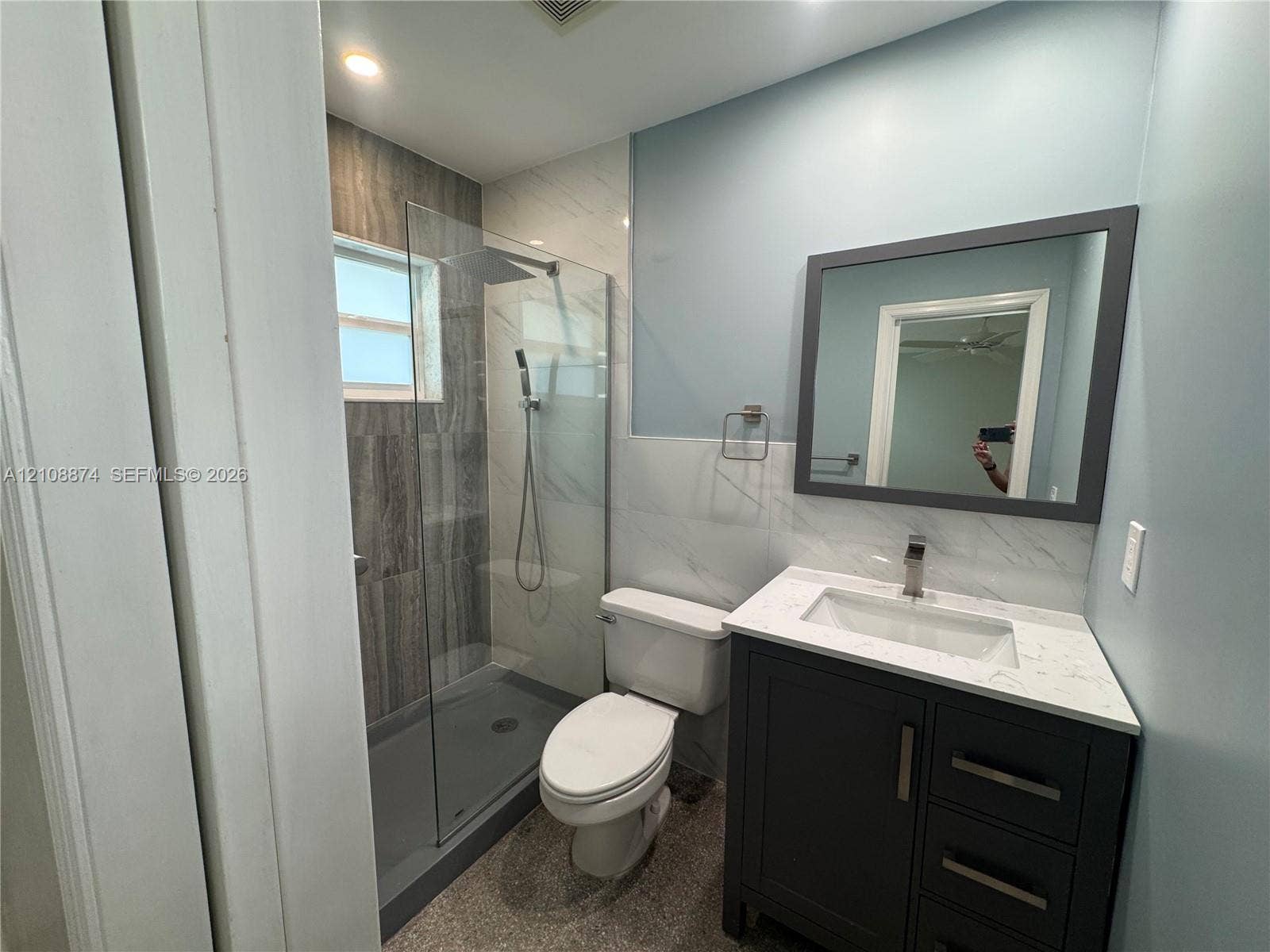 Bathroom featuring a dark vanity with a white countertop and rectangular undermount sink, walk-in shower with floor-to-ceiling tile, glass enclosure, and a wall-mounted rectangular mirror